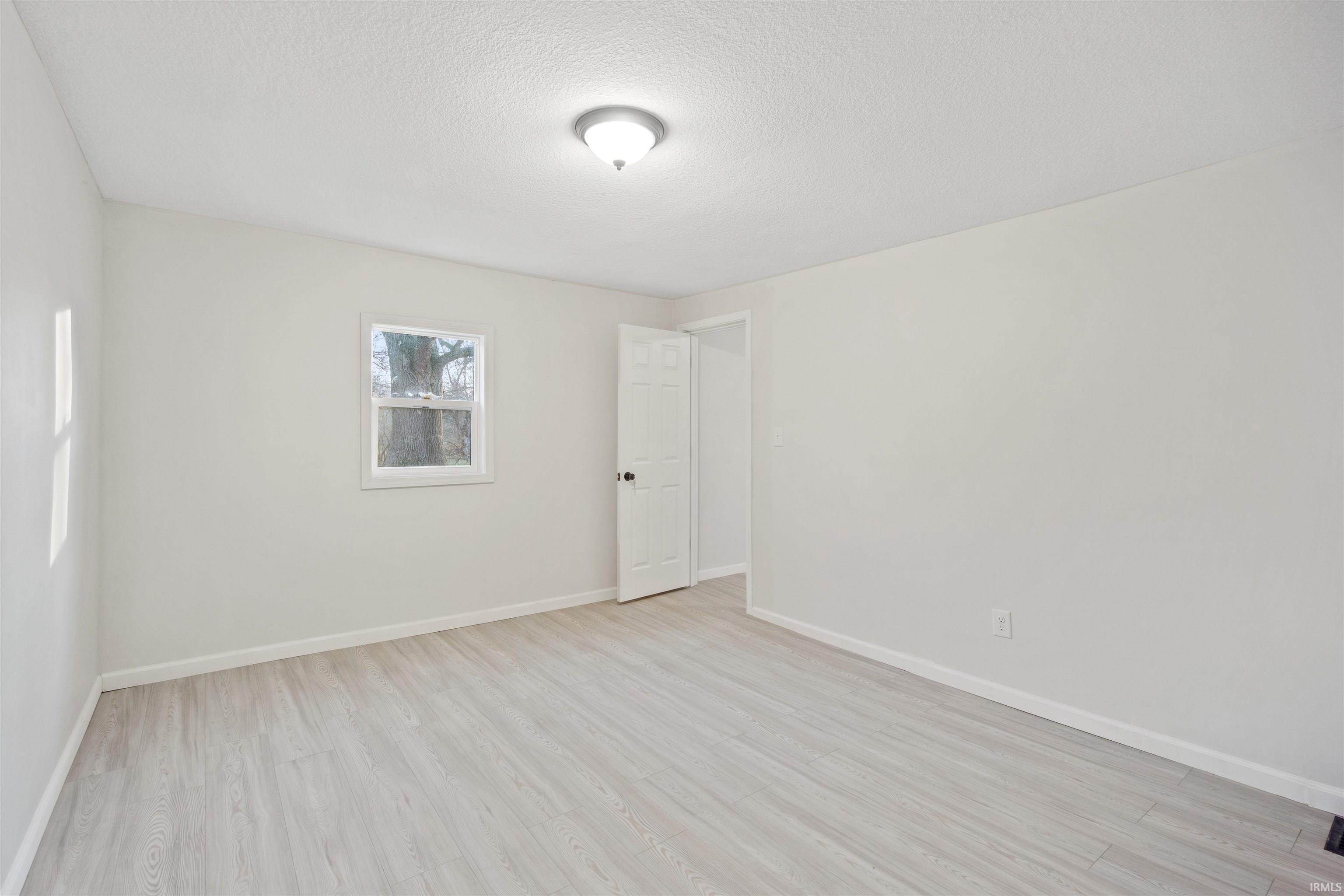 Empty room with light wood-type flooring and a textured ceiling