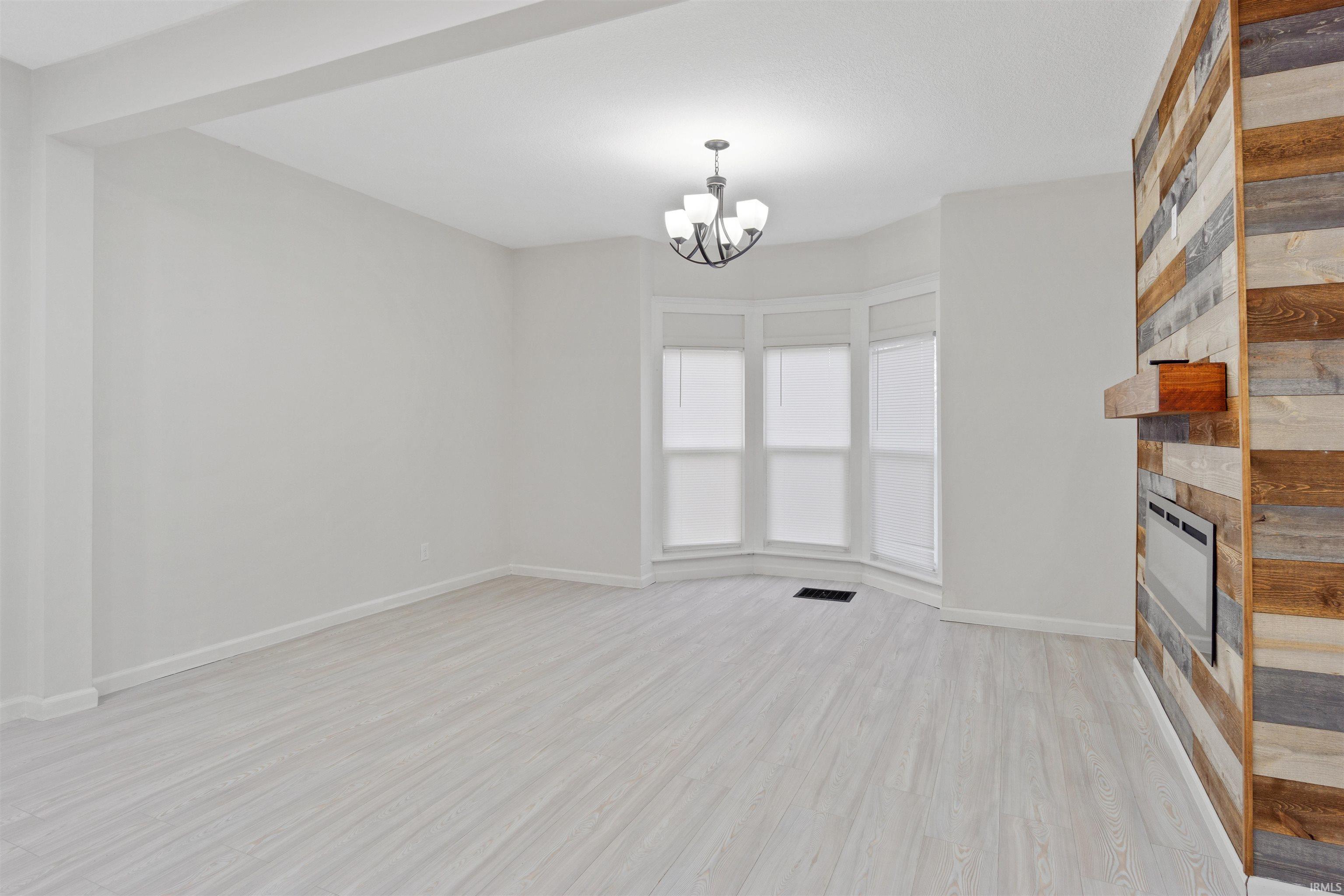 Unfurnished living room with a large fireplace, light wood-style floors, and a chandelier