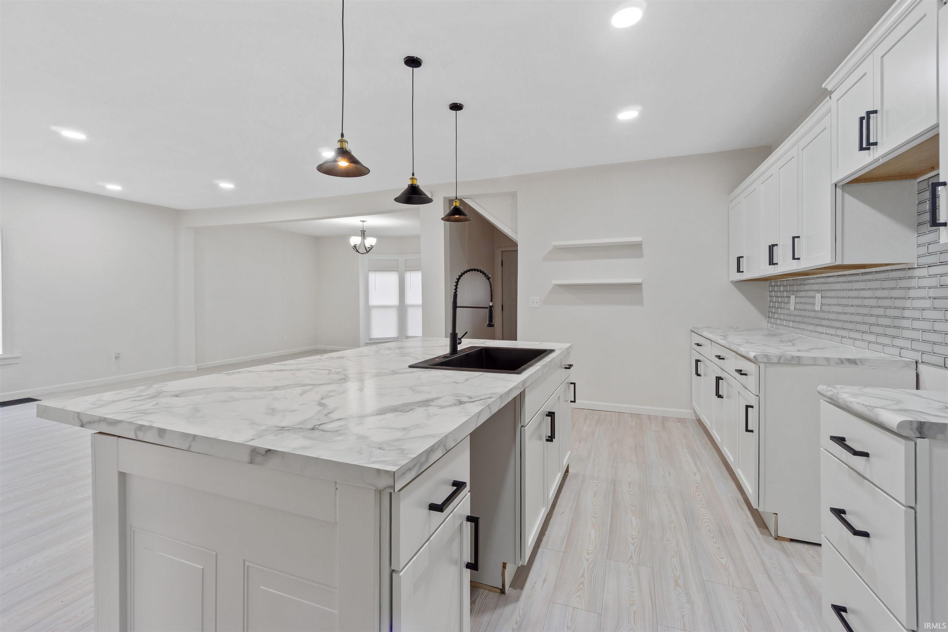 Kitchen featuring white cabinetry, a kitchen island with sink, decorative backsplash, light wood-style floors, and hanging light fixtures