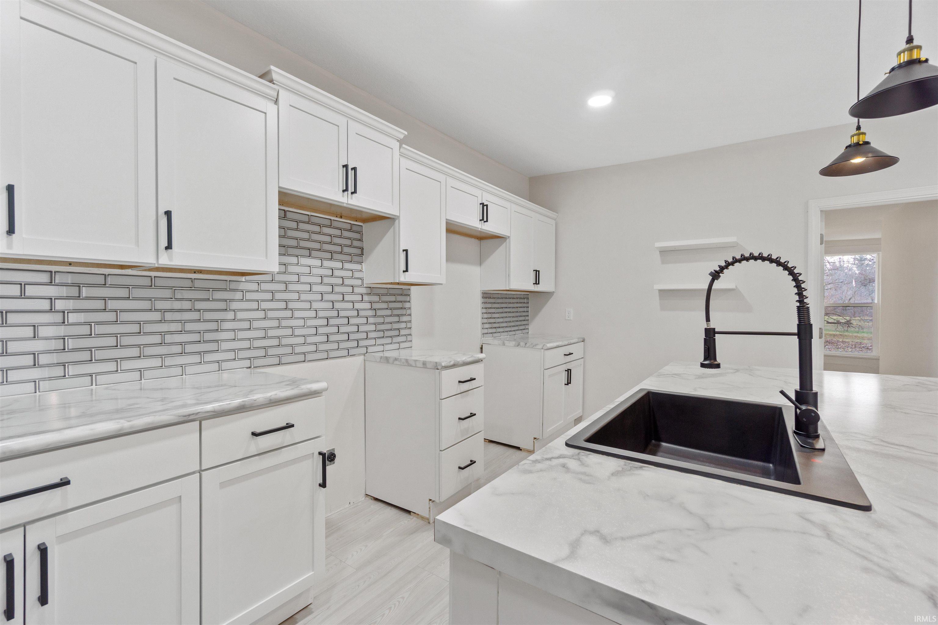 Kitchen featuring white cabinetry, backsplash, decorative light fixtures, light stone countertops, and recessed lighting