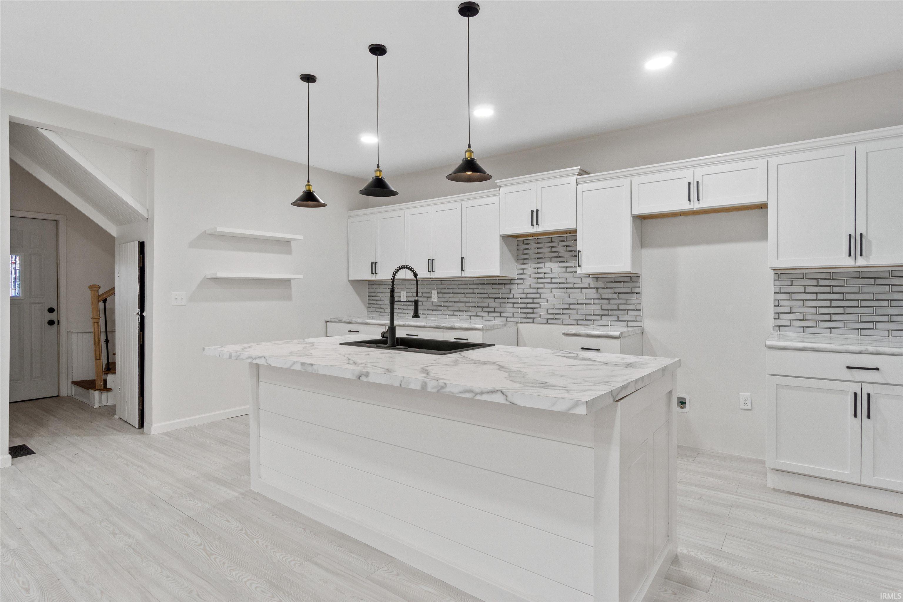 Kitchen featuring white cabinetry, decorative backsplash, hanging light fixtures, an island with sink, and light wood finished floors