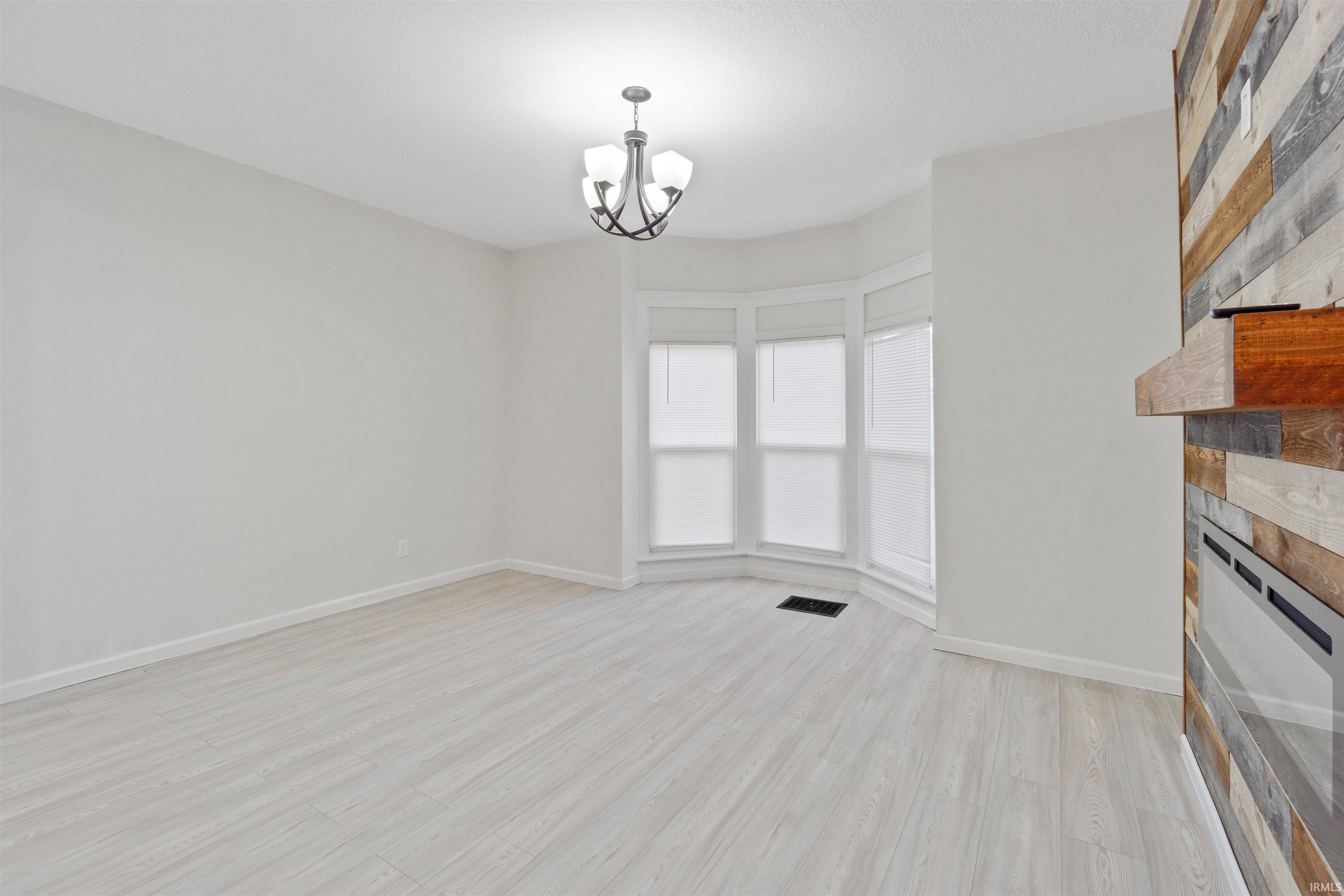 Unfurnished living room with light wood finished floors, a chandelier, and a fireplace