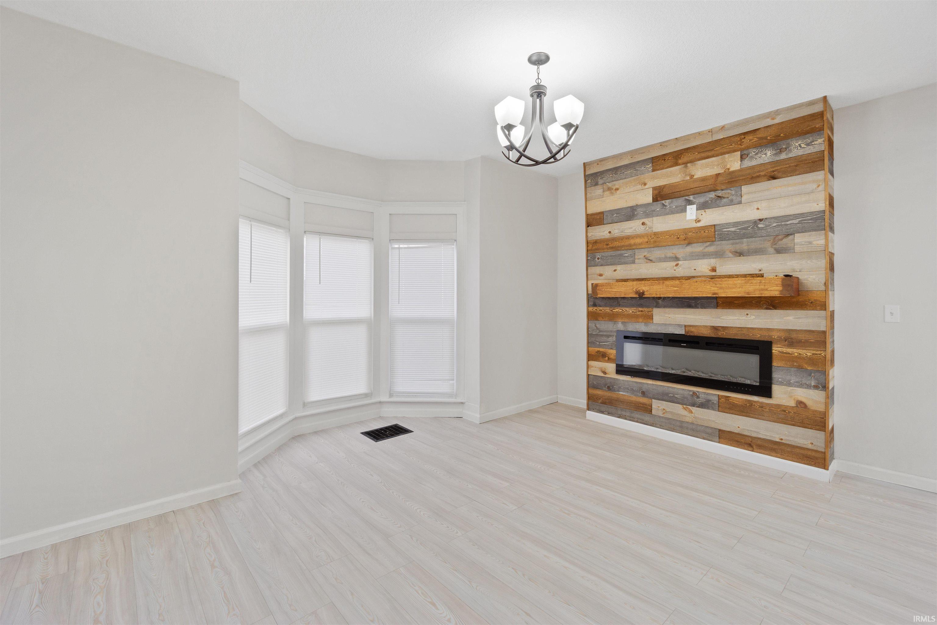 Unfurnished living room with light wood-style flooring, a chandelier, and a glass covered fireplace
