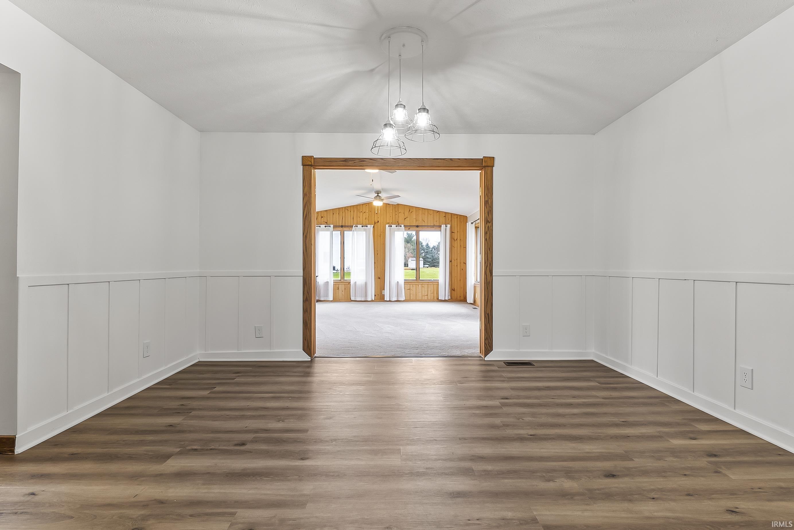 Unfurnished room with wainscoting, a chandelier, dark wood-type flooring, vaulted ceiling, and a ceiling fan