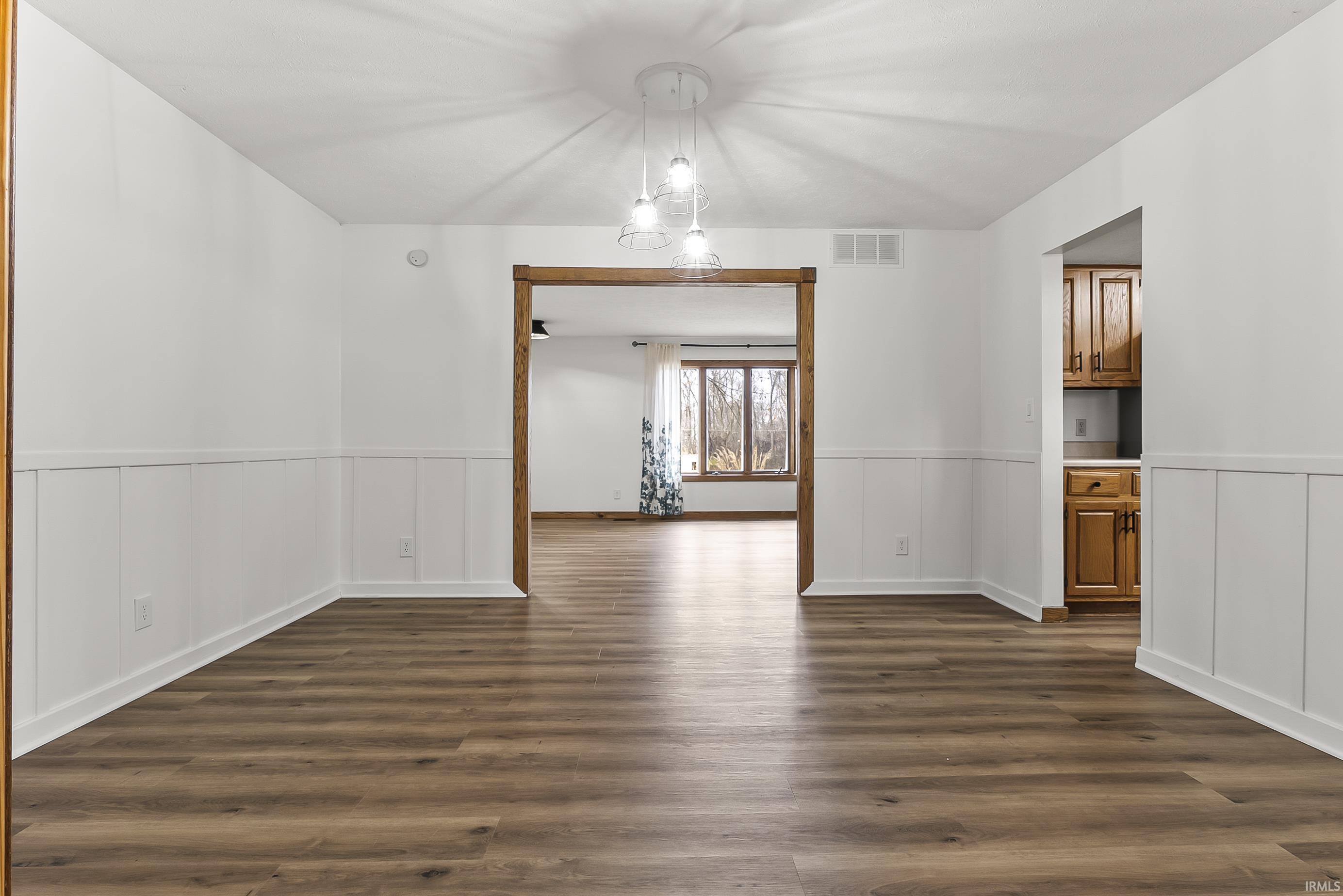 Unfurnished dining area featuring dark wood-style floors and wainscoting