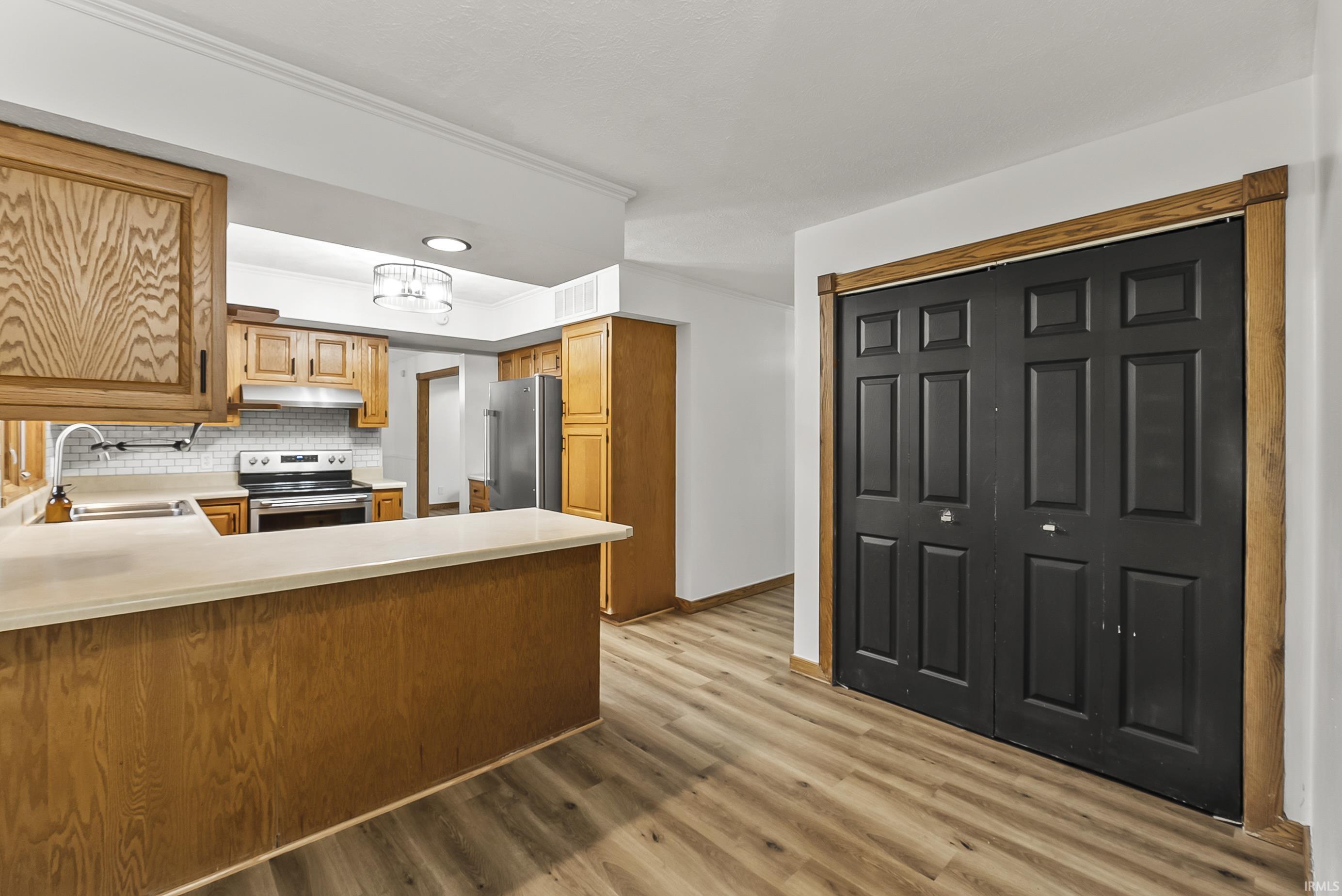 Kitchen with light countertops, appliances with stainless steel finishes, a peninsula, decorative backsplash, and light wood-type flooring