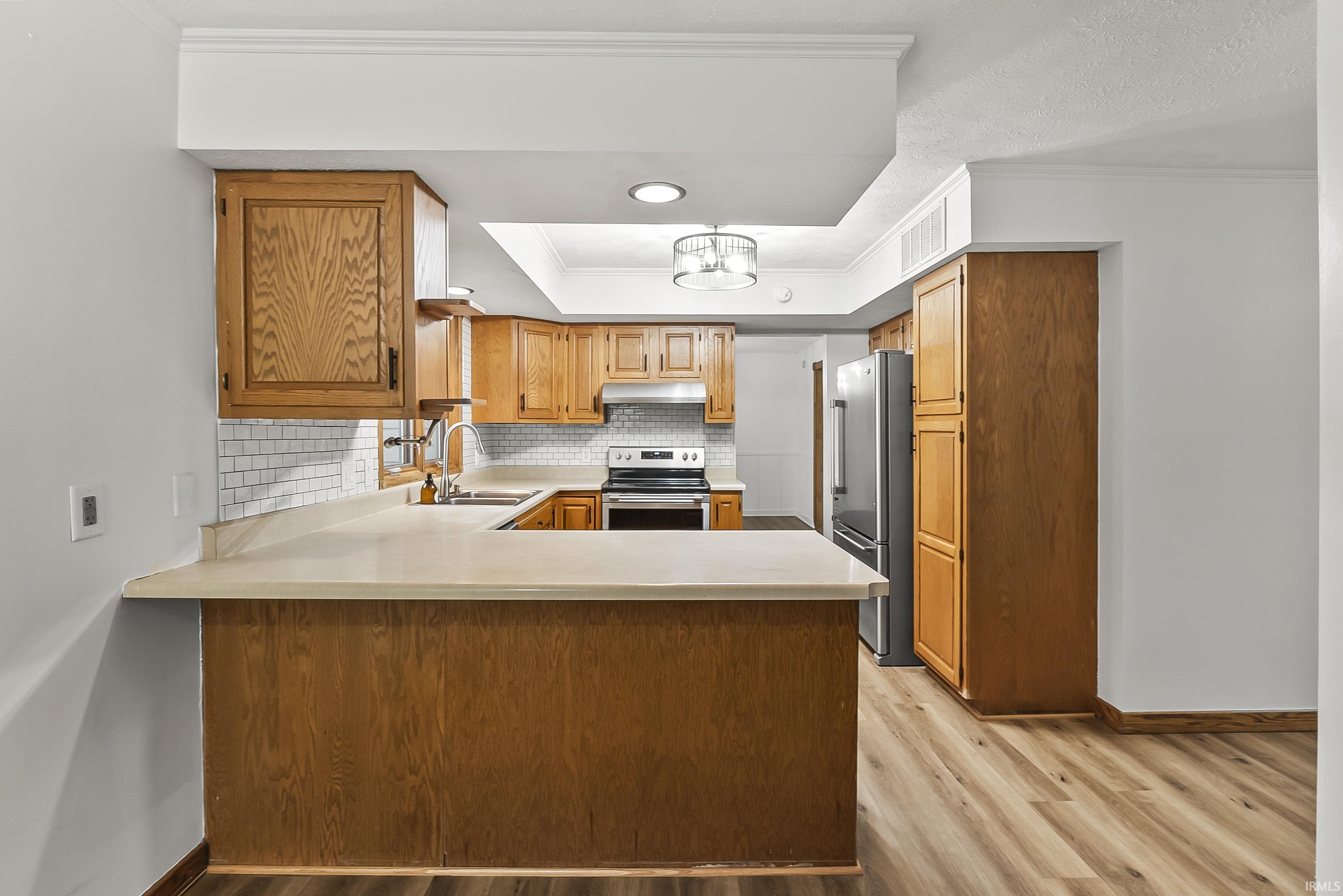 Kitchen with crown molding, a peninsula, light countertops, stainless steel appliances, and decorative backsplash