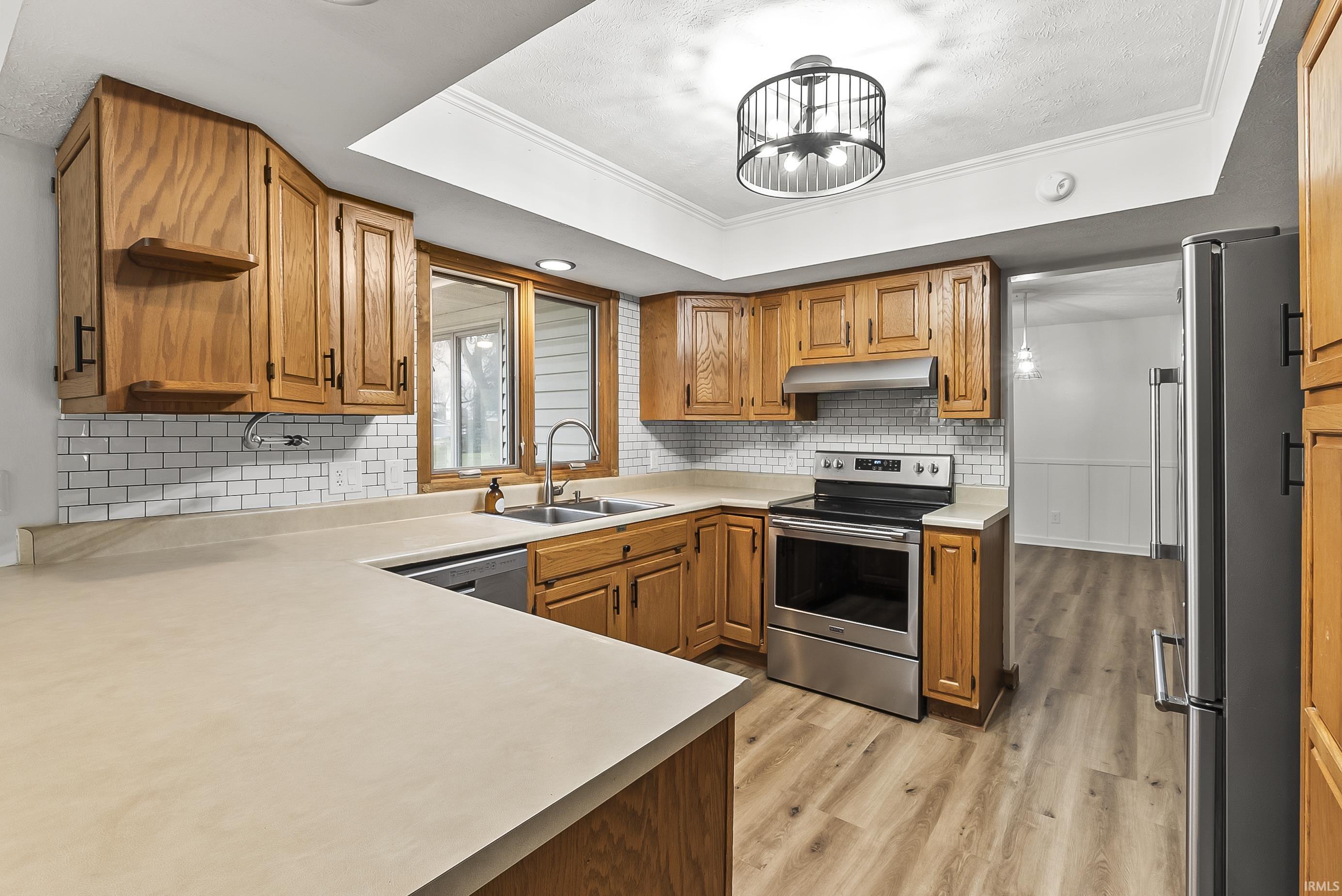 Kitchen with stainless steel appliances, brown cabinets, ornamental molding, light countertops, and light wood-type flooring