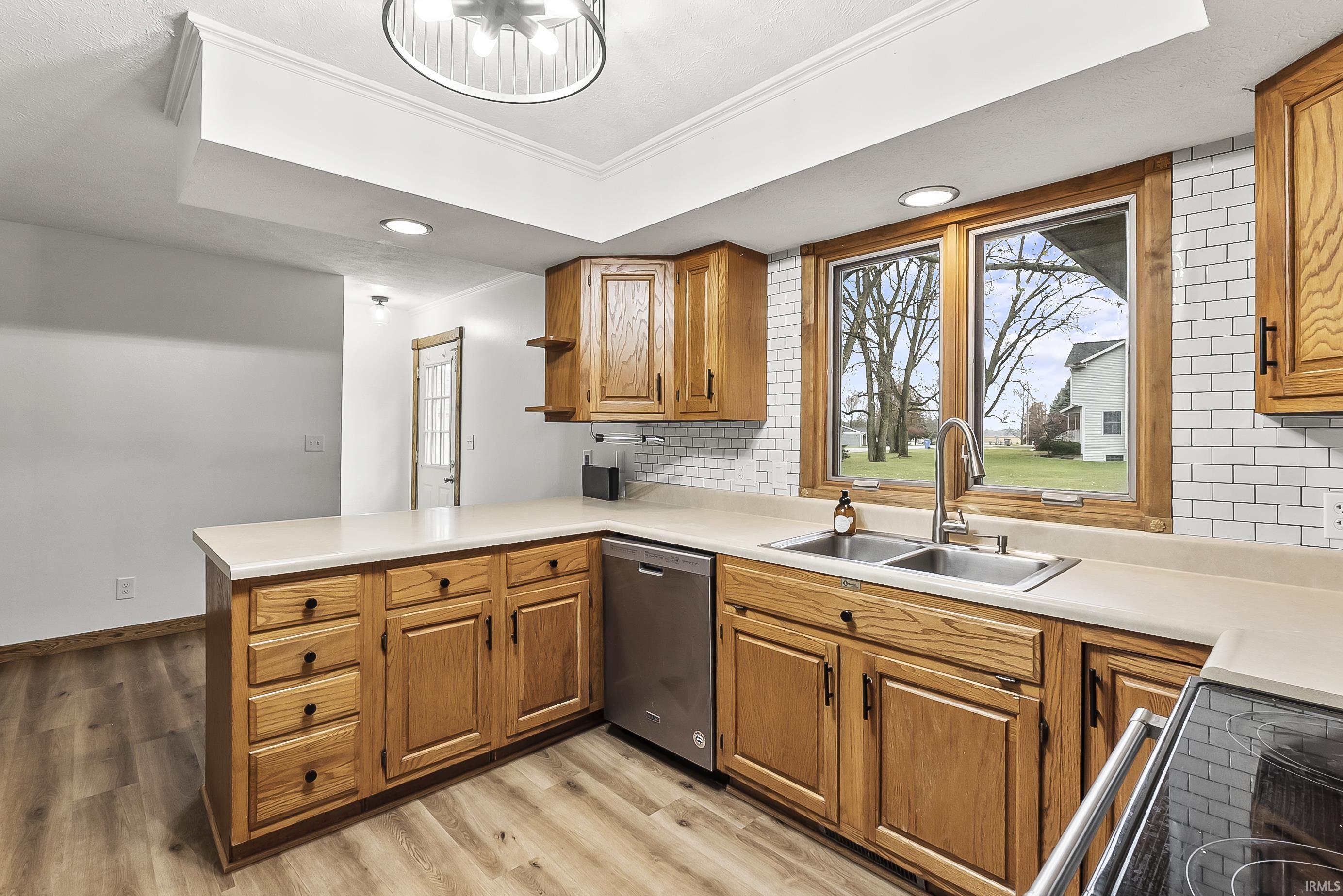 Kitchen with decorative backsplash, brown cabinets, a peninsula, black electric range oven, and light countertops