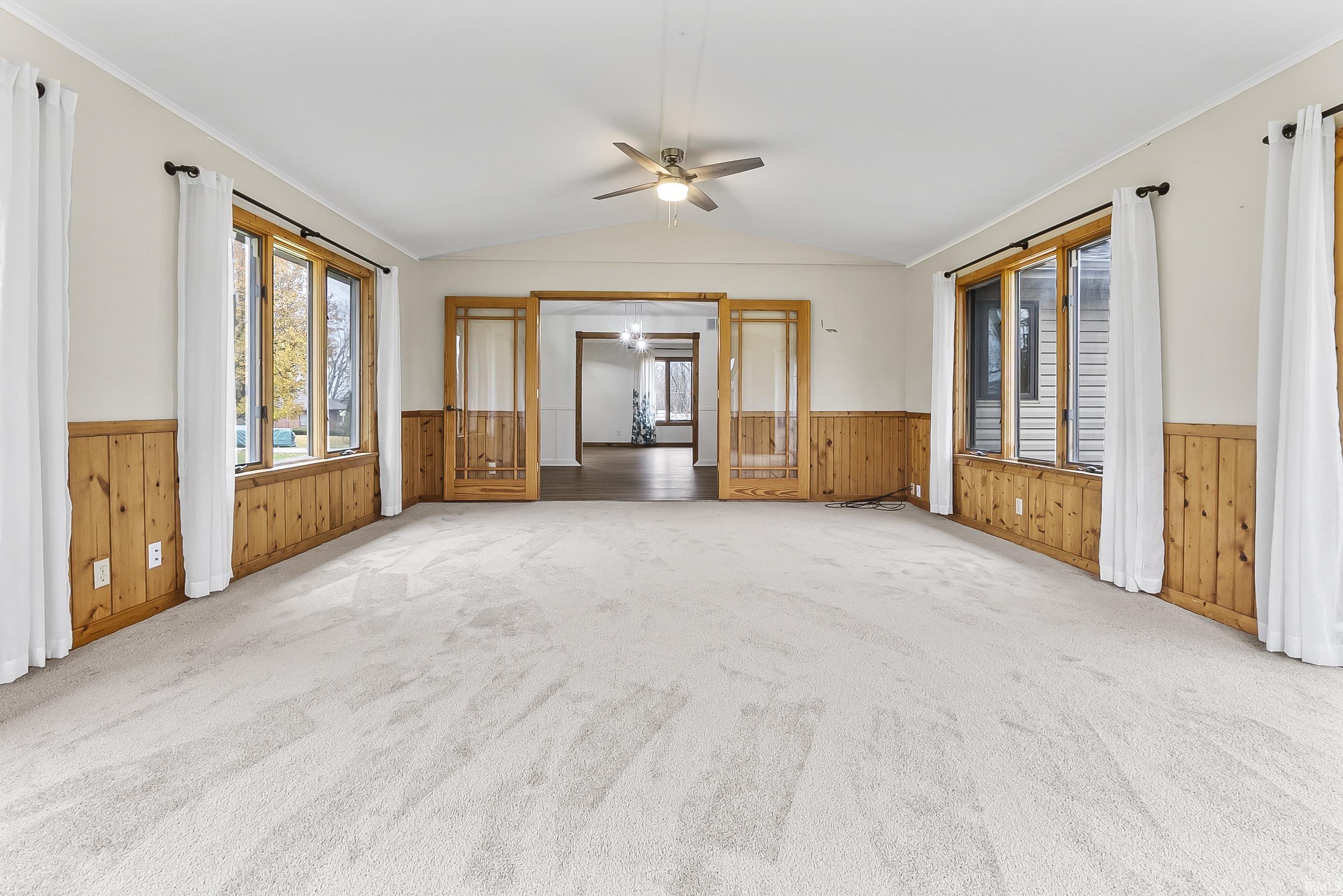 Unfurnished living room with a ceiling fan, vaulted ceiling, a wainscoted wall, carpet flooring, and ornamental molding