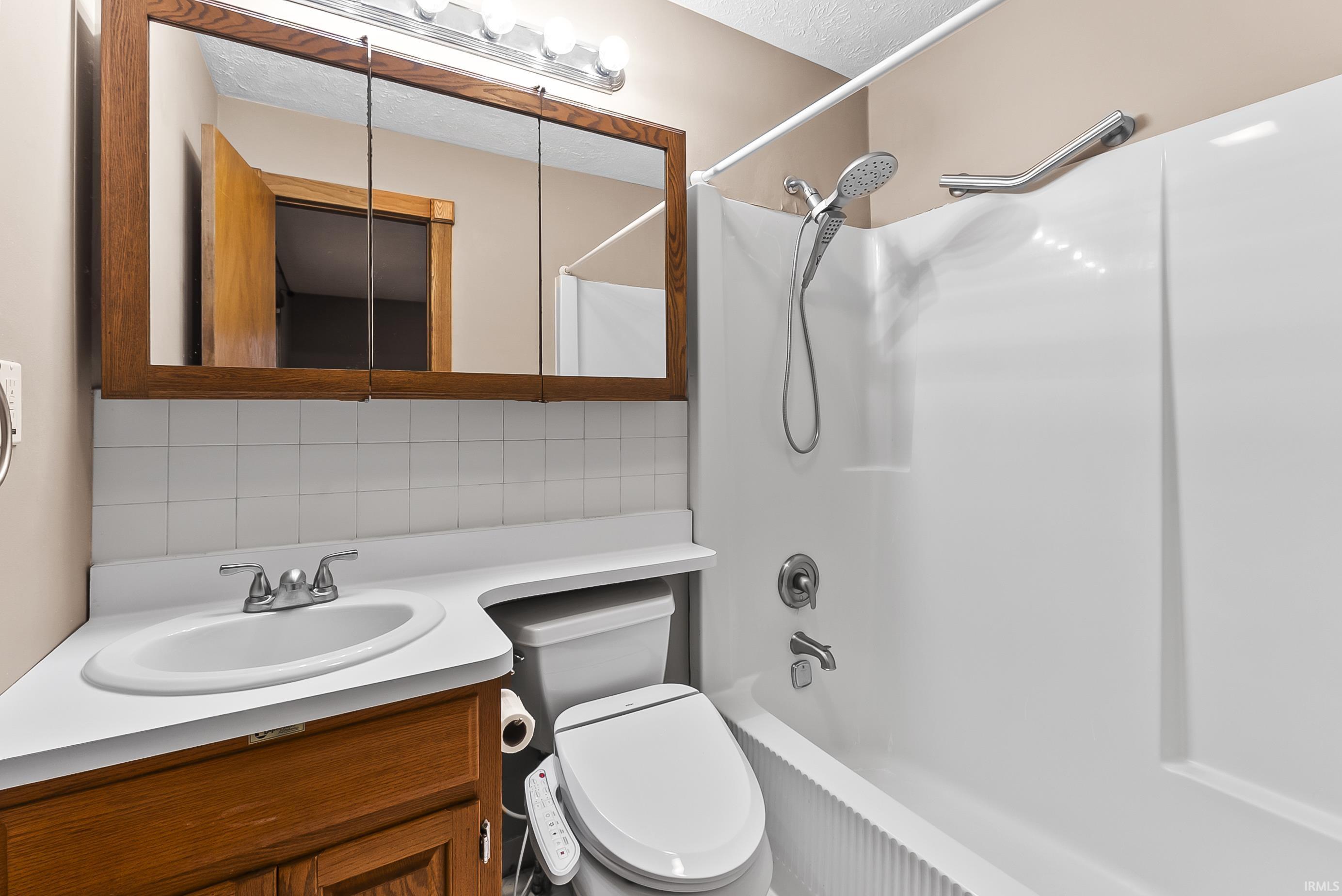 Bathroom with backsplash, vanity, shower / washtub combination, and a textured ceiling