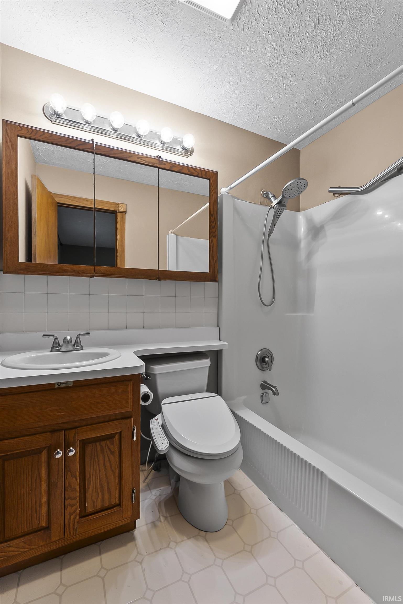 Bathroom featuring bathing tub / shower combination, vanity, a textured ceiling, and backsplash