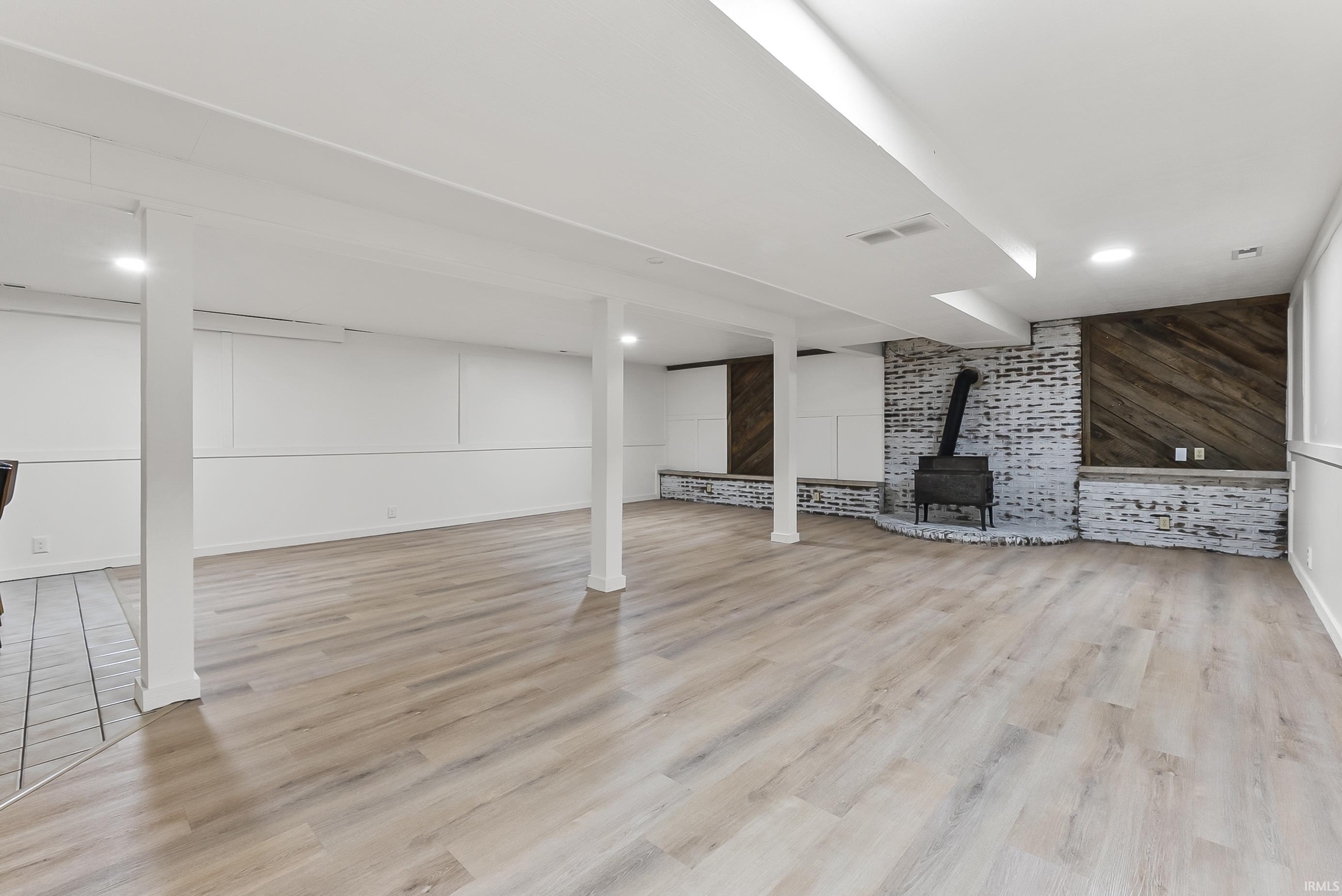 Finished below grade area featuring wooden walls, light wood-style flooring, a wood stove, an accent wall, and recessed lighting