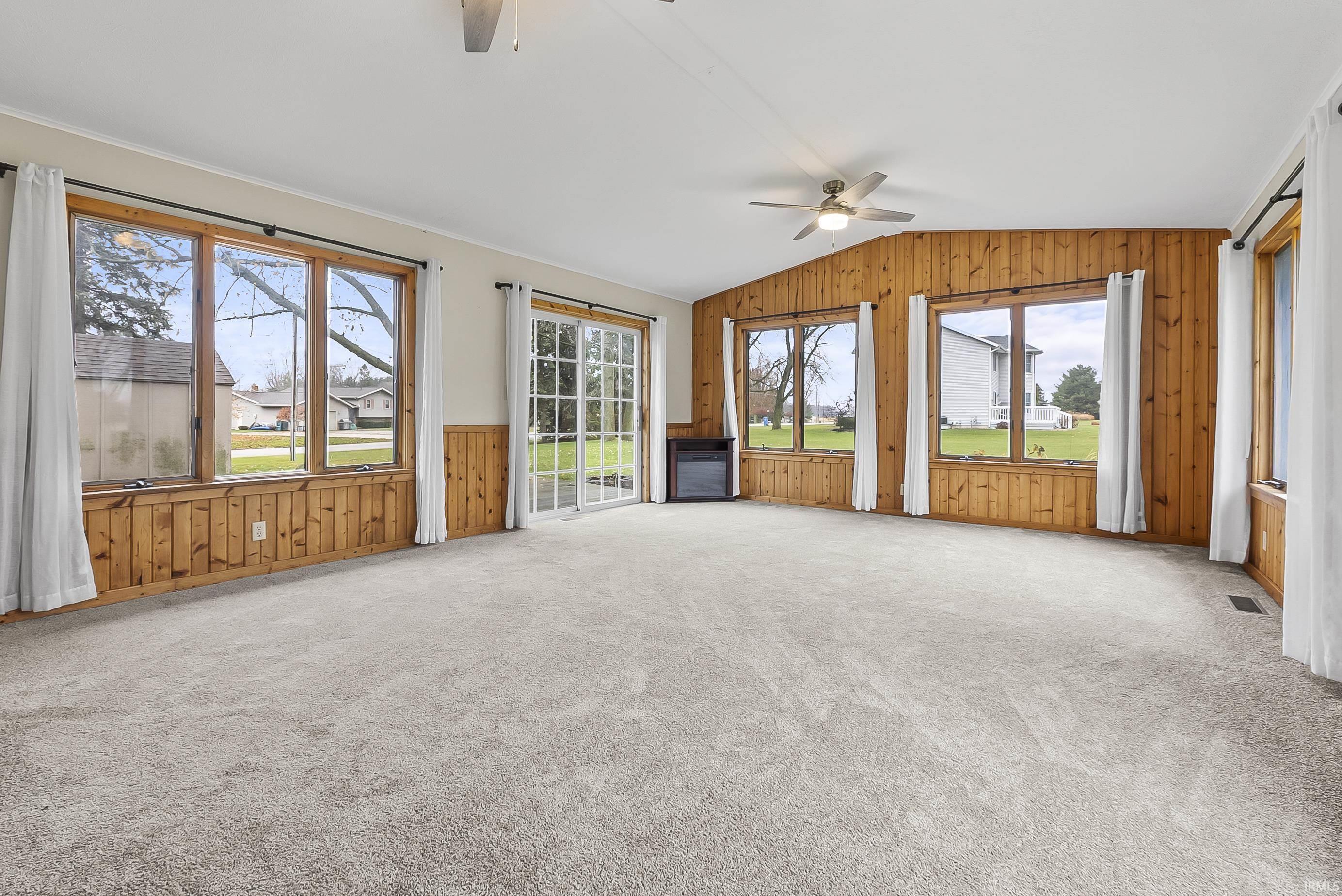 Unfurnished living room with wooden walls, vaulted ceiling, ceiling fan, and light carpet