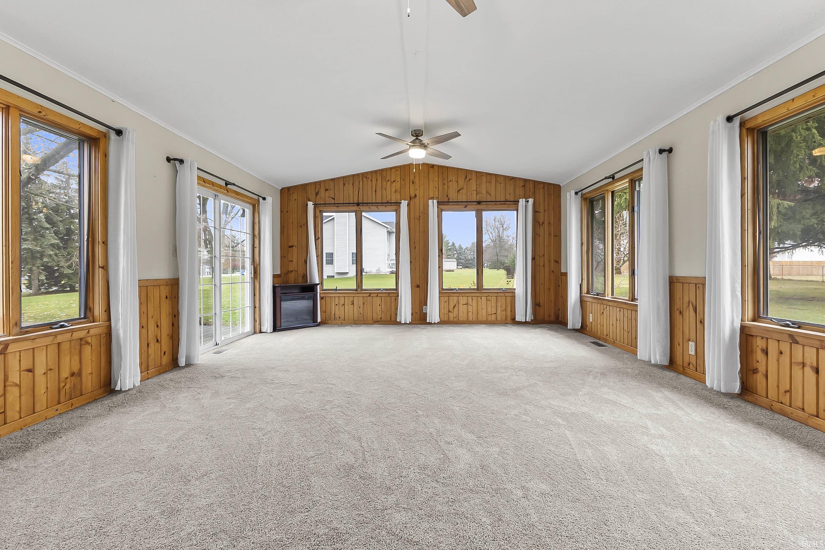 Unfurnished living room featuring wooden walls, lofted ceiling, a wainscoted wall, plenty of natural light, and a ceiling fan