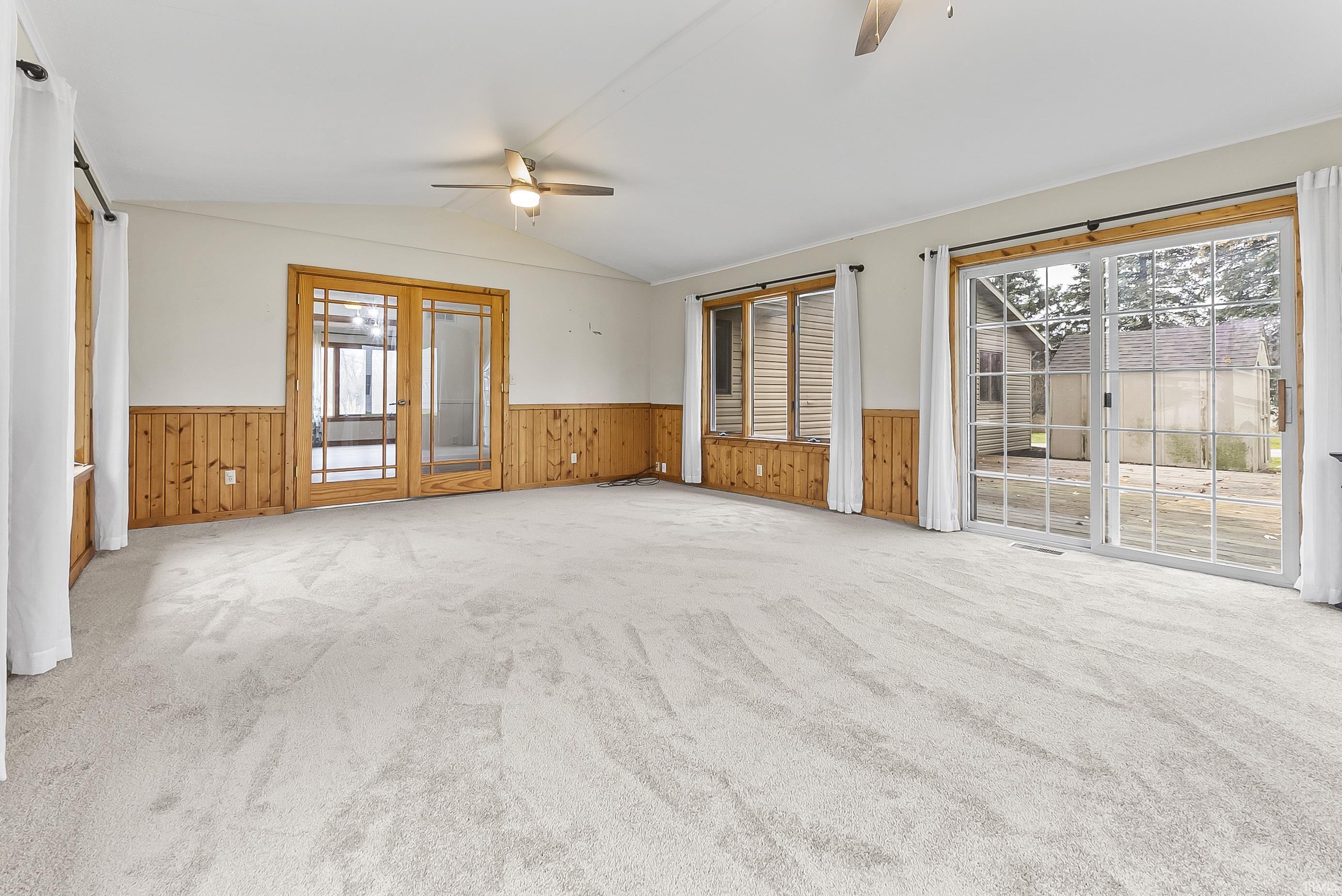 Spare room with light carpet, ceiling fan, wooden walls, vaulted ceiling, and wainscoting