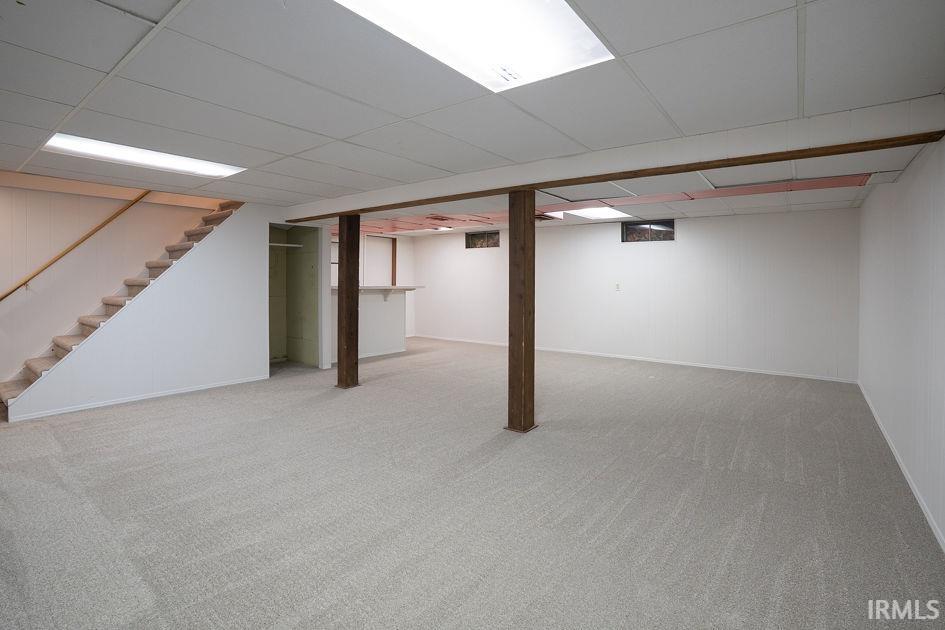 Finished basement with a drop ceiling and light colored carpet