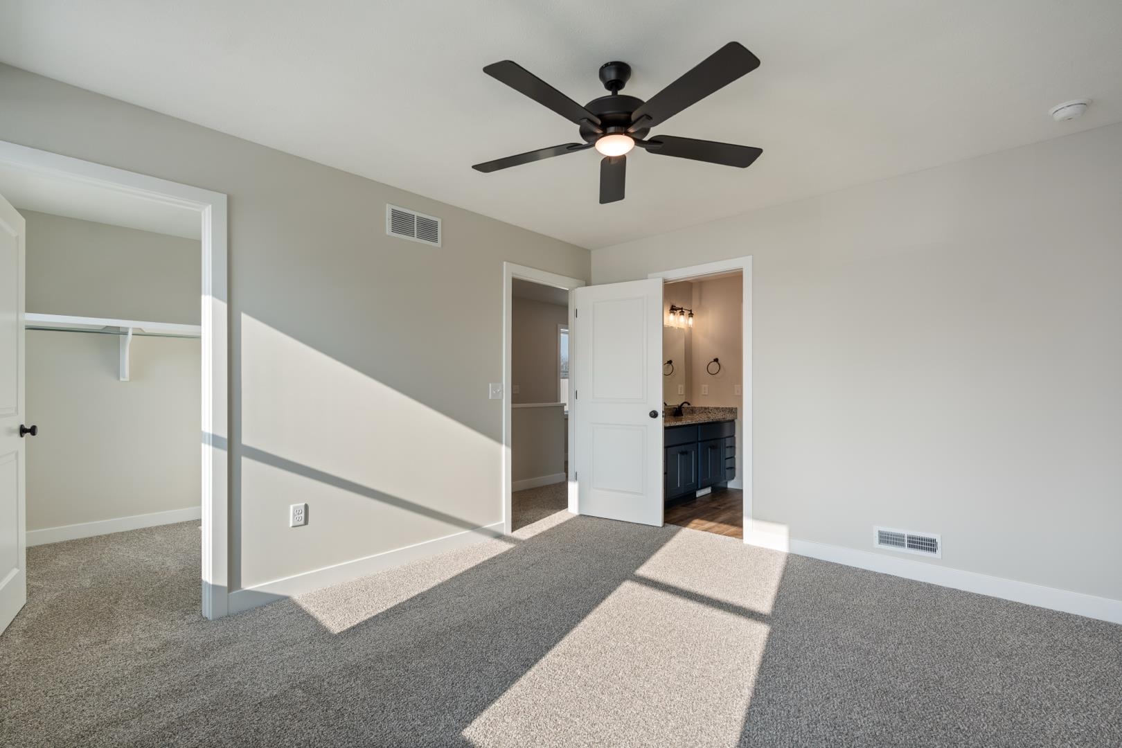 Unfurnished bedroom featuring a spacious closet, light colored carpet, ceiling fan, and ensuite bath
