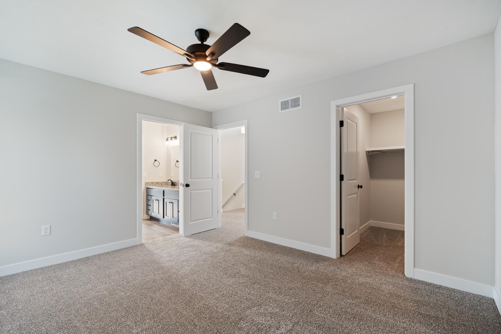 Unfurnished bedroom featuring light carpet, a walk in closet, and a ceiling fan