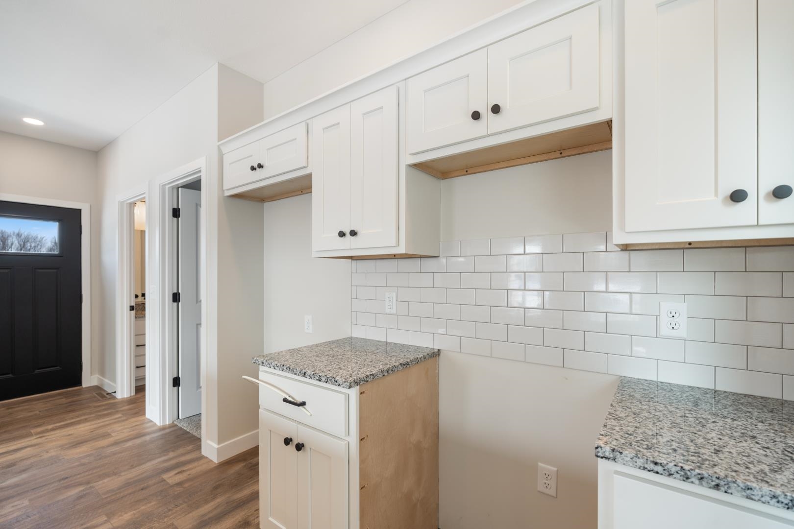 Kitchen featuring white cabinets, light stone counters, tasteful backsplash, and dark wood-type flooring - Appliances will be coming