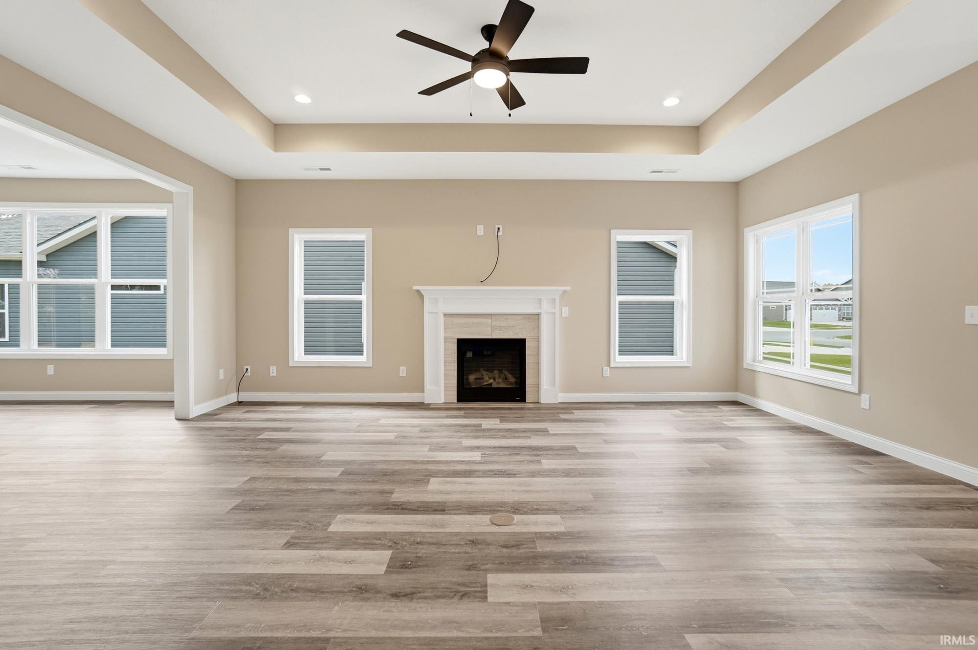 Unfurnished living room with a tray ceiling, ceiling fan, light wood finished floors, and a tiled fireplace