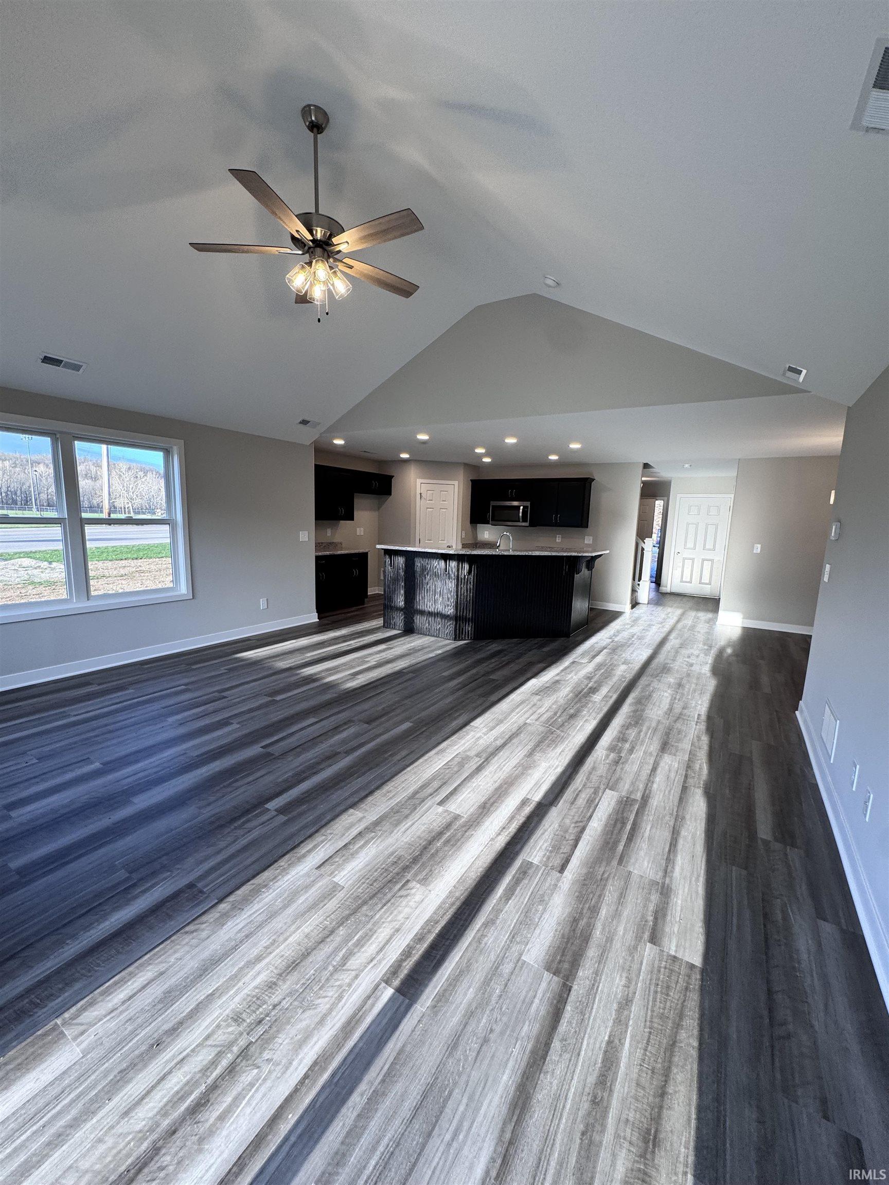Unfurnished living room featuring a ceiling fan, healthy amount of natural light, and dark wood-type flooring