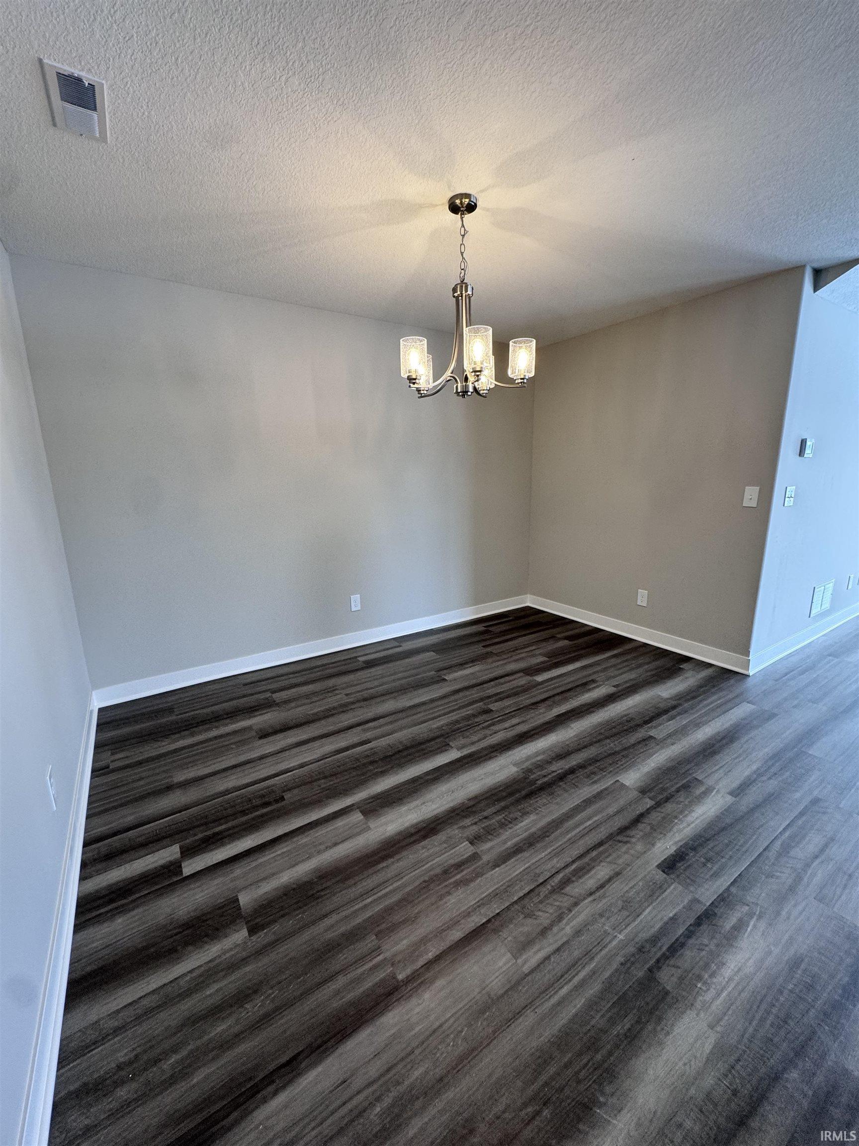 Unfurnished dining area with hanging lights, a textured ceiling, and dark wood-type flooring
