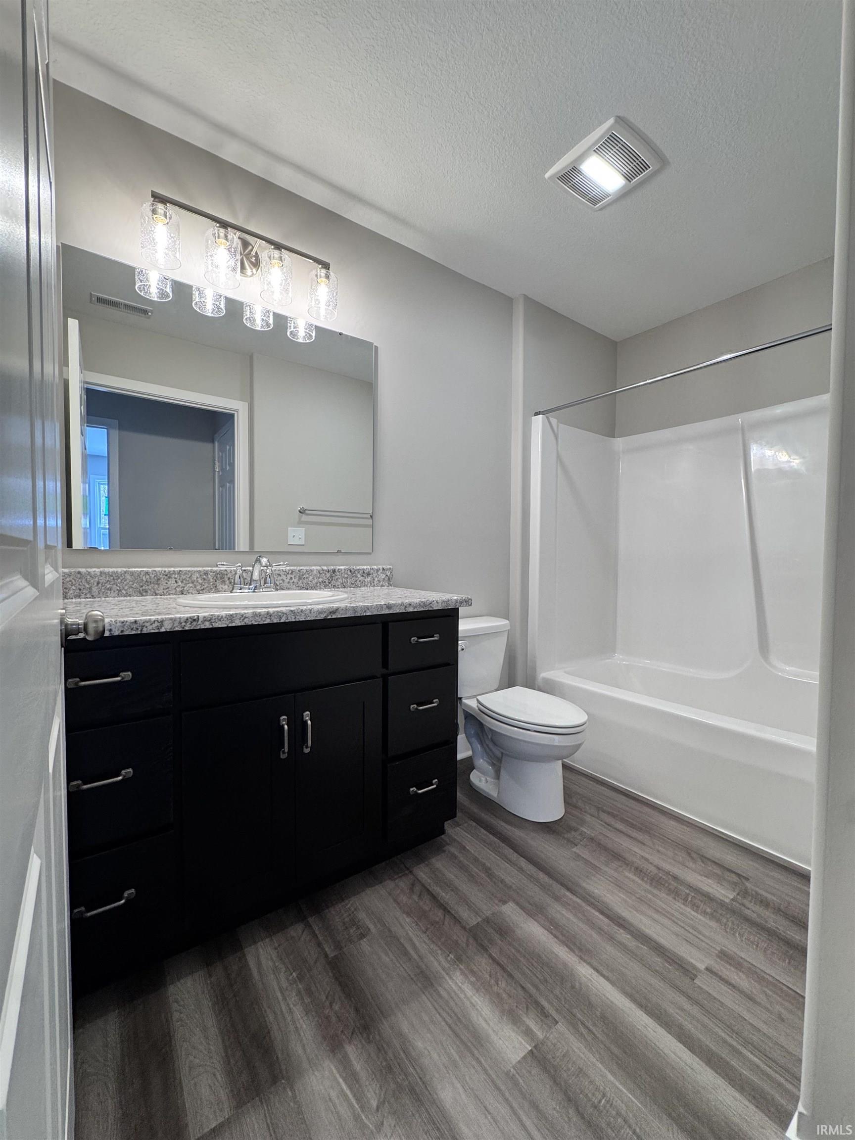 Bathroom featuring vanity, dark wood-style flooring, washtub / shower combination, and a textured ceiling
