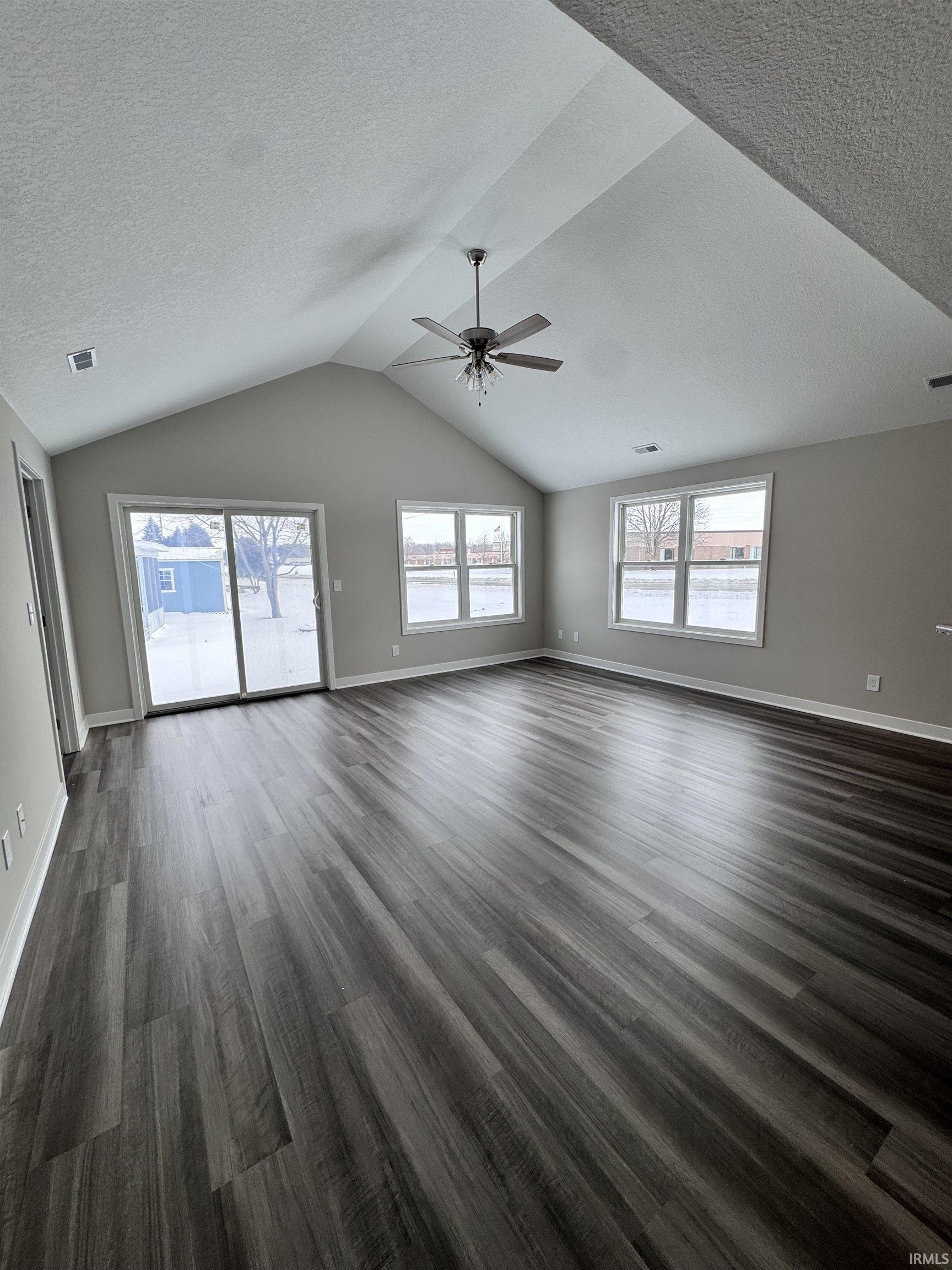 Unfurnished living room featuring a textured ceiling, a ceiling fan, and dark wood finished floors