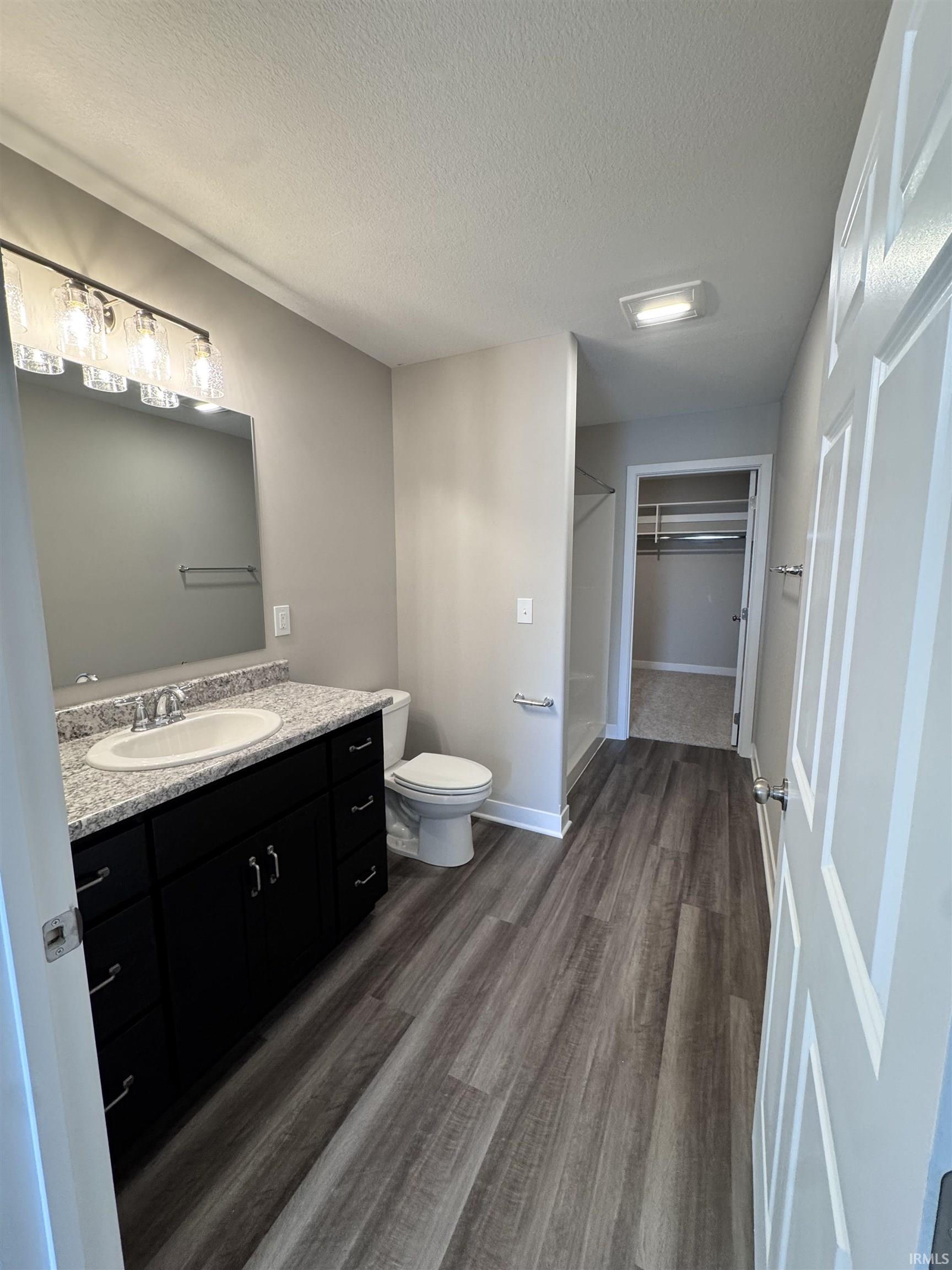 Full bathroom featuring a spacious closet, vanity, a shower stall, dark wood-style floors, and a textured ceiling