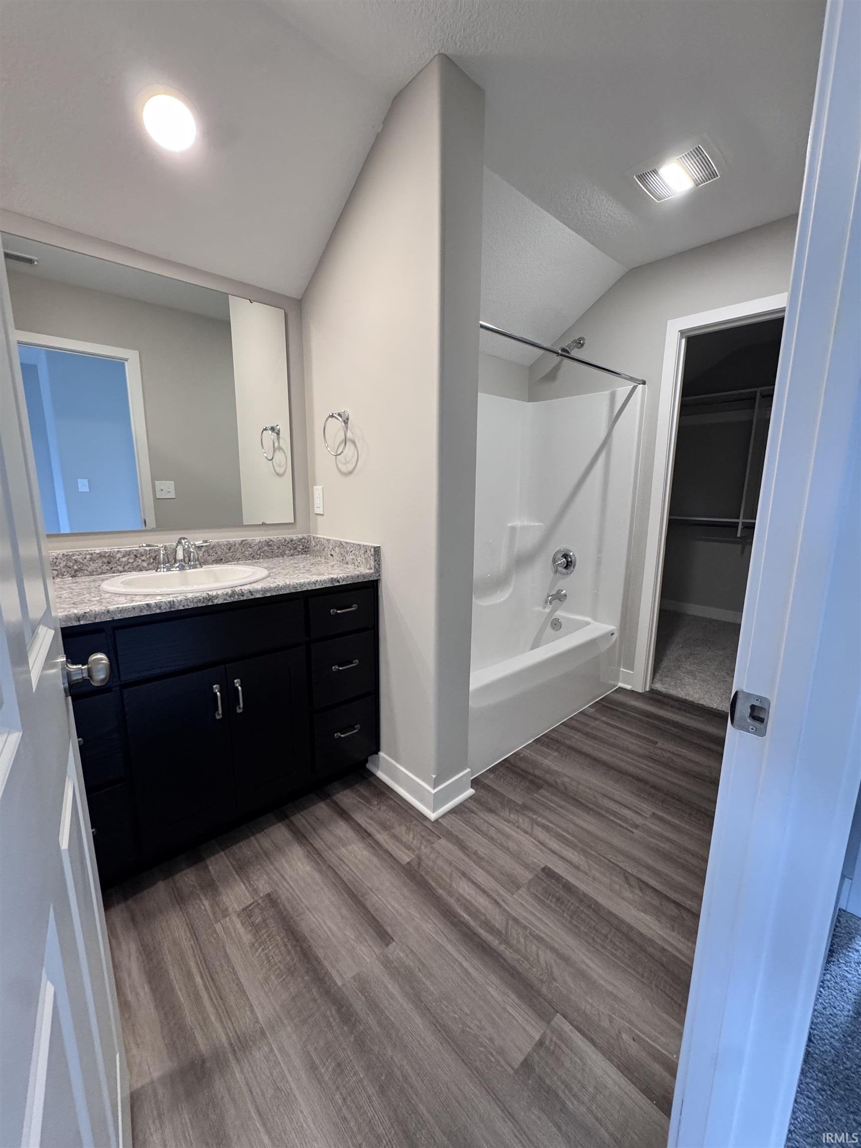 Bathroom featuring a walk in closet, vanity,  shower combination, dark wood-style flooring, and vaulted ceiling