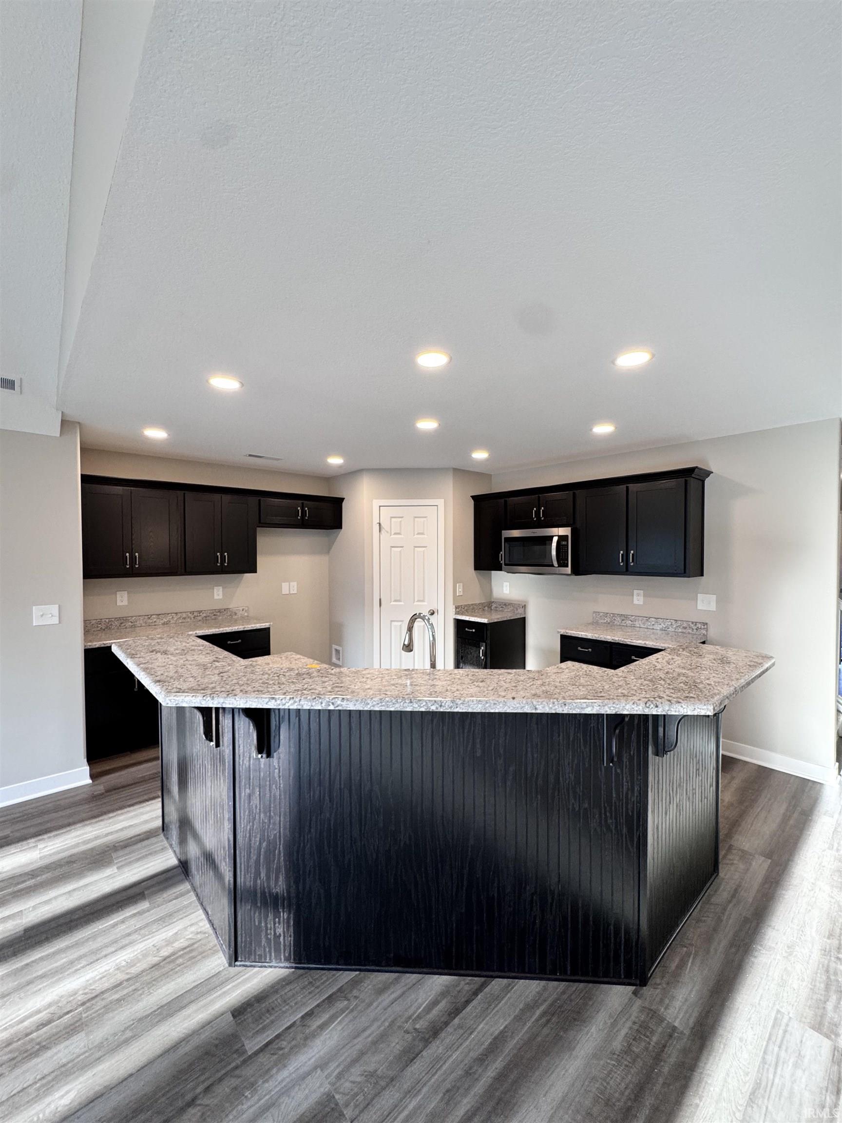 Kitchen featuring a breakfast bar area, light stone countertops, and dark cabinetry