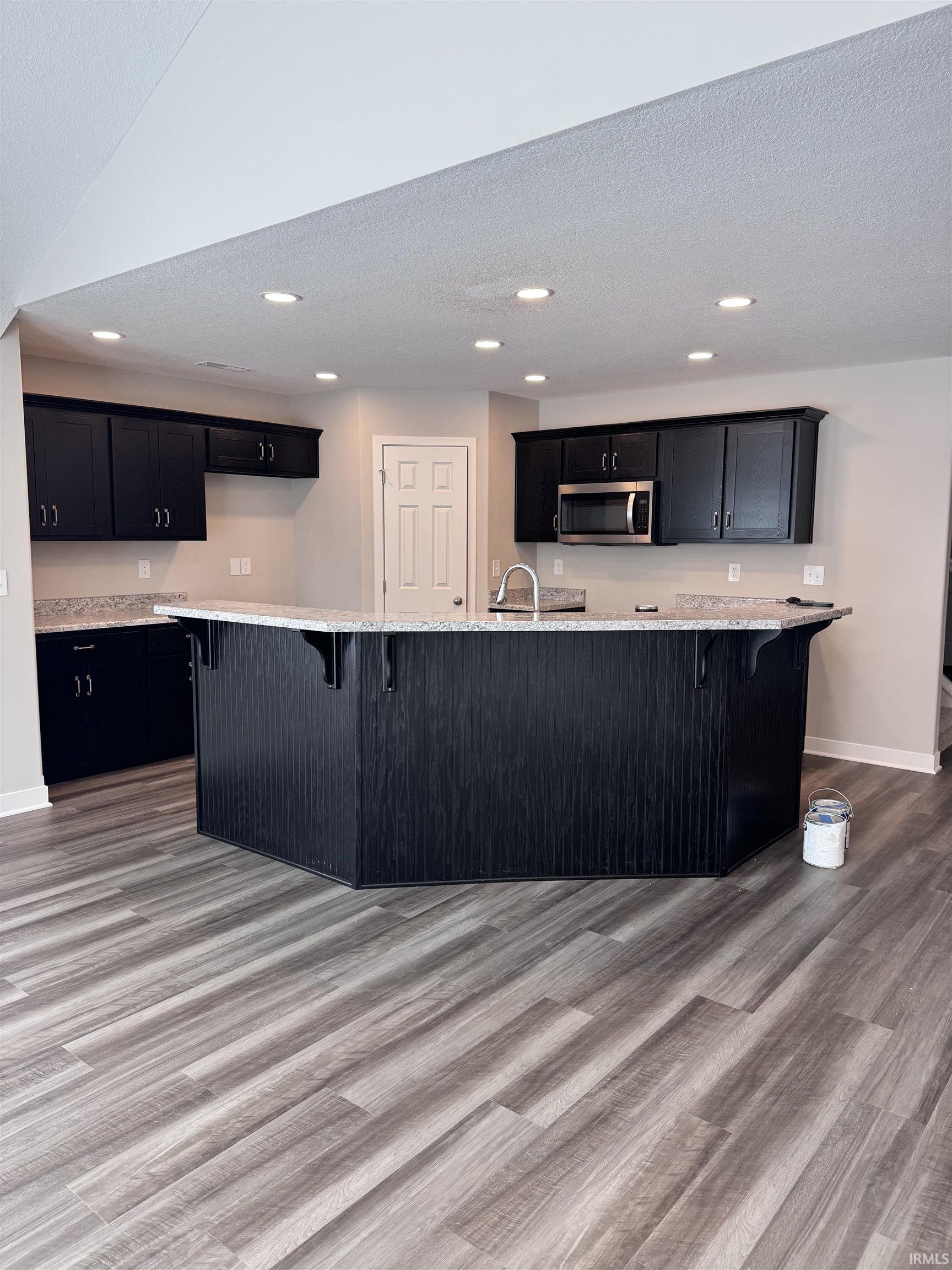Kitchen featuring a kitchen breakfast bar, dark cabinetry, light wood-style floors, stainless steel microwave, and a textured ceiling