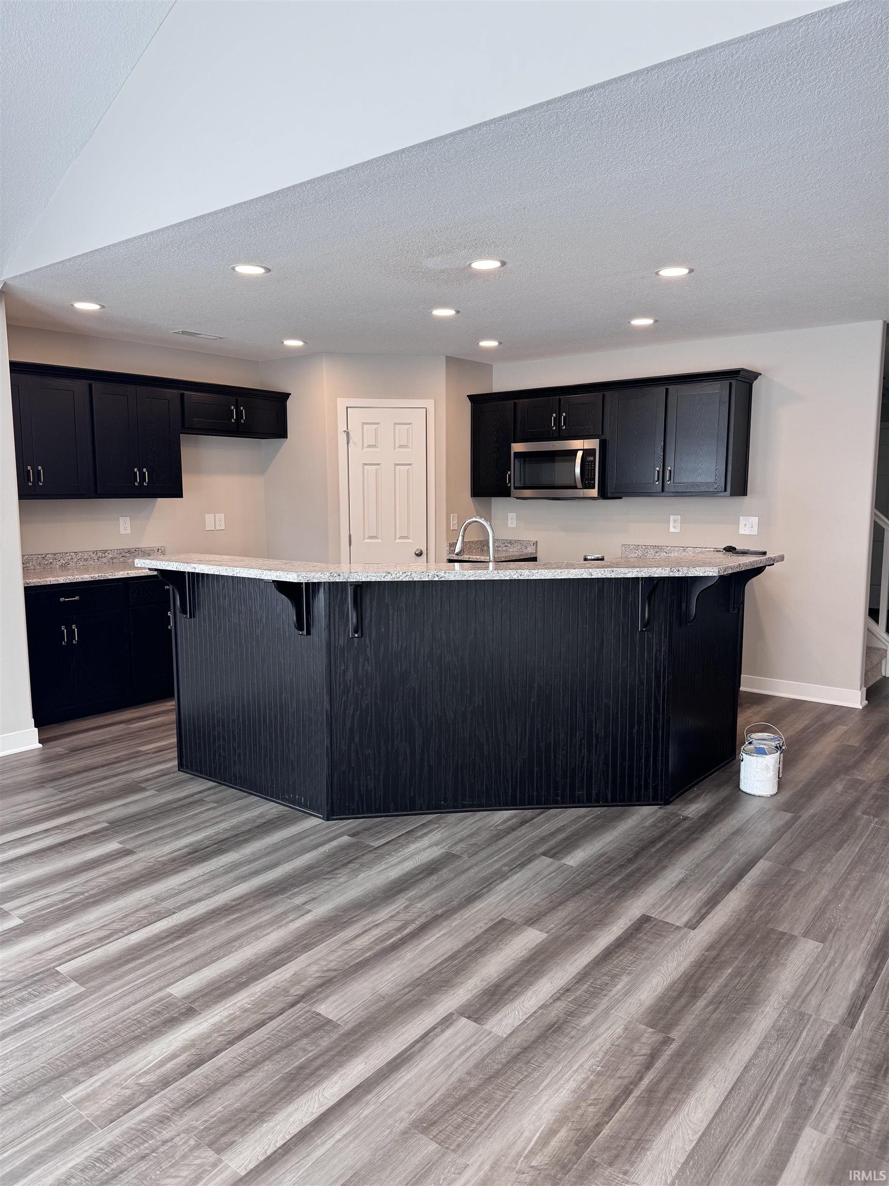 Kitchen with a kitchen breakfast bar, dark cabinets, light wood finished floors, recessed lighting, and a textured ceiling