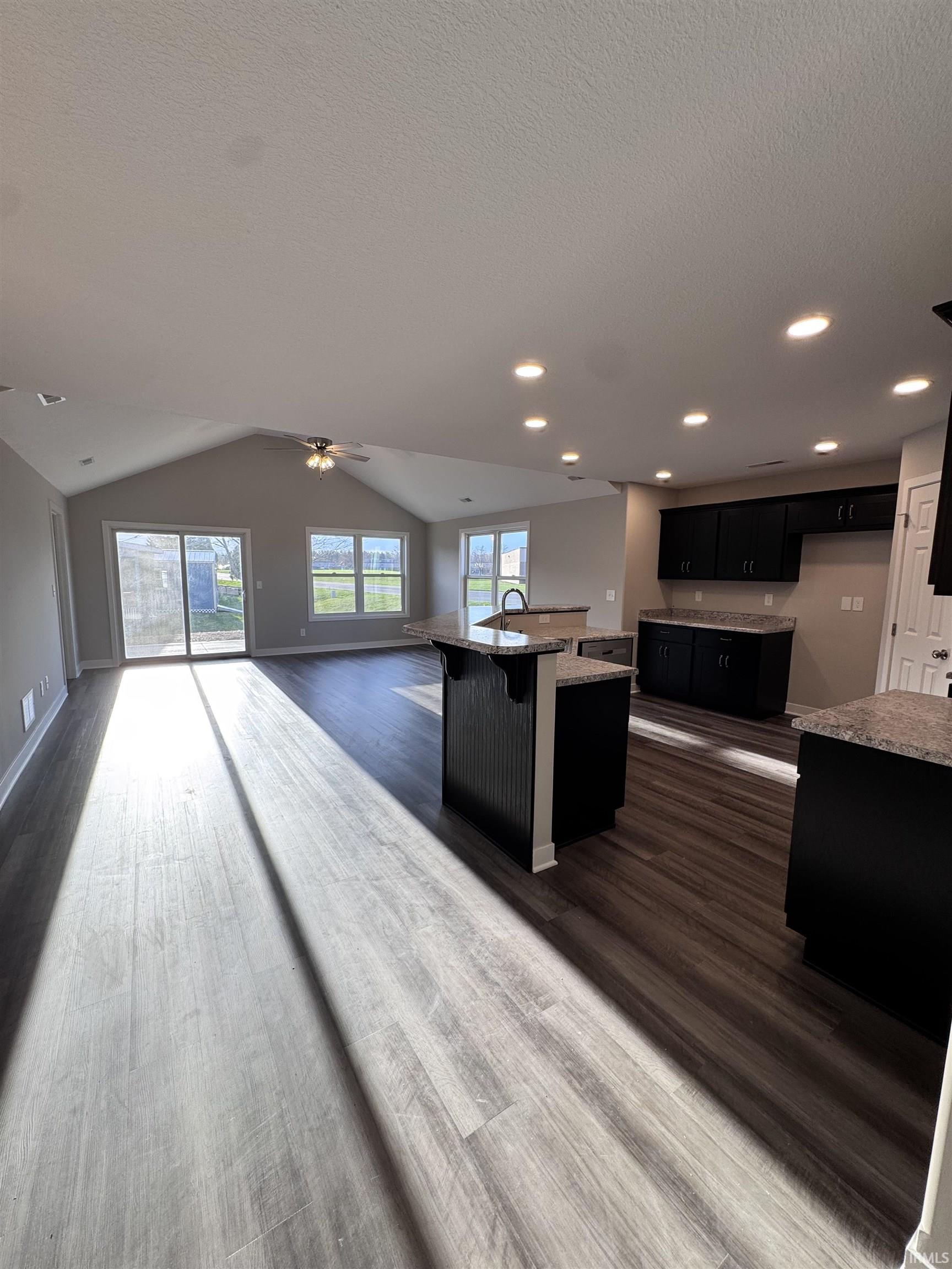 Kitchen with dark cabinetry, a center island with sink, open floor plan, a breakfast bar, and dark wood-style floors