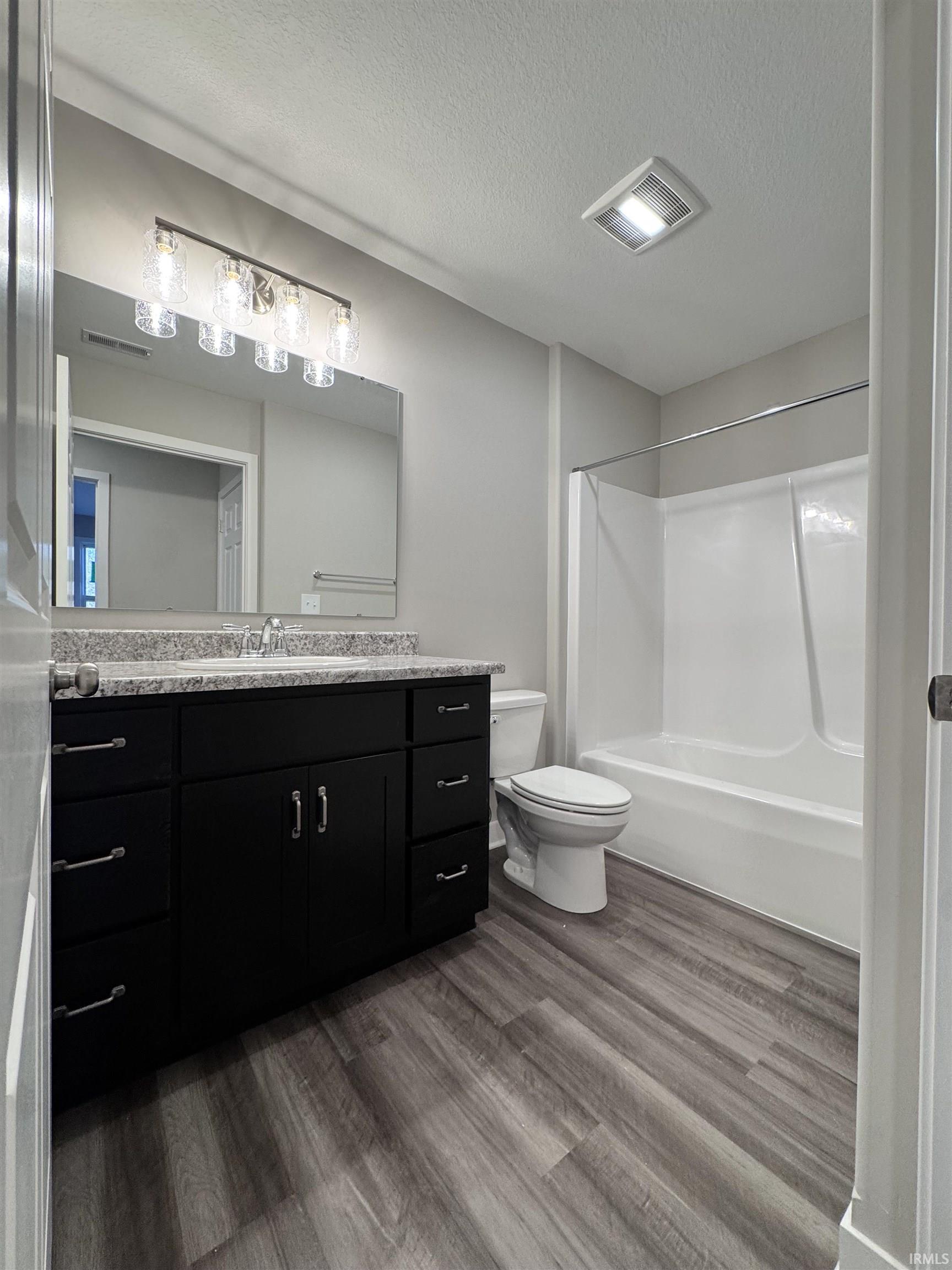 Bathroom featuring vanity, dark wood-type flooring, a textured ceiling, and shower / bath combination