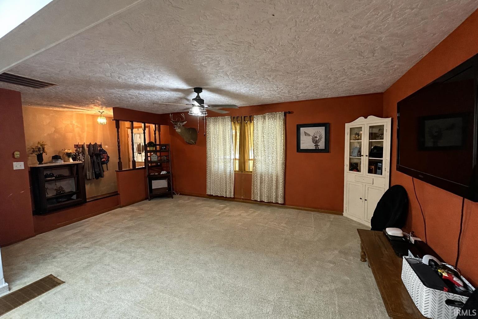 Unfurnished living room with light colored carpet, a textured ceiling, and a ceiling fan