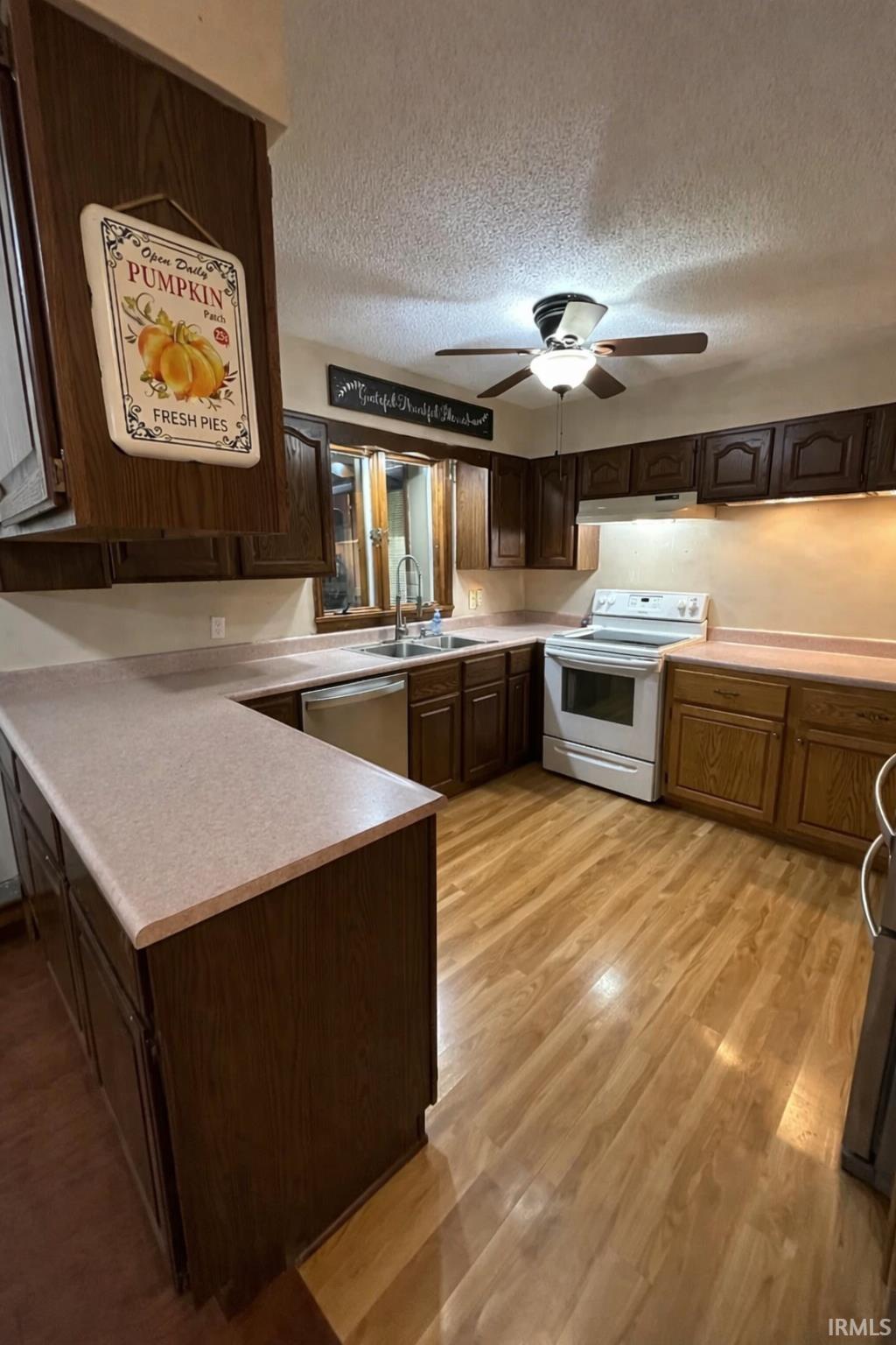 Kitchen with a textured ceiling, stainless steel appliances, light countertops, dark wood finish cabinetry, and light wood-type flooring