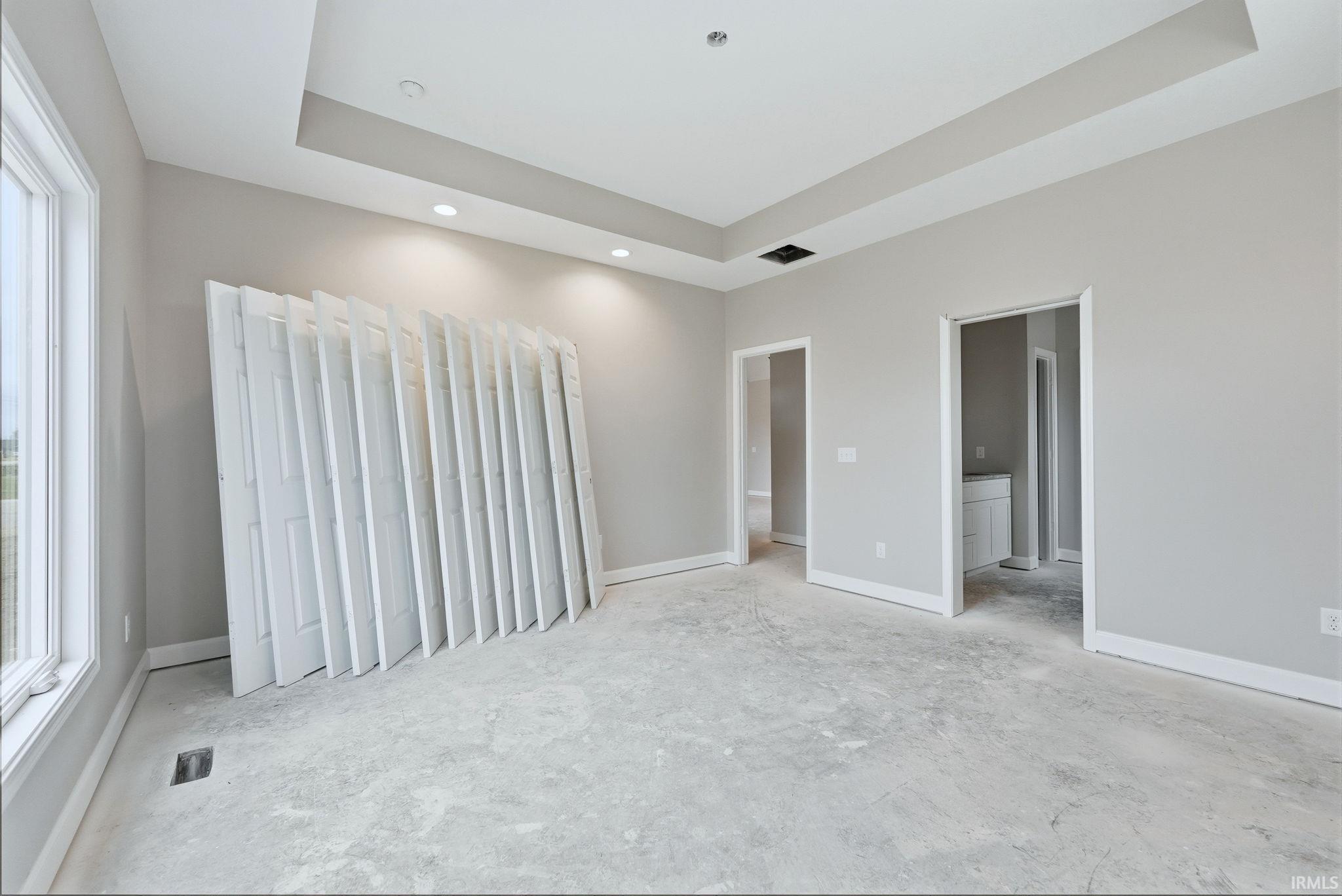 Unfurnished bedroom with a tray ceiling, recessed lighting, and ensuite bathroom
