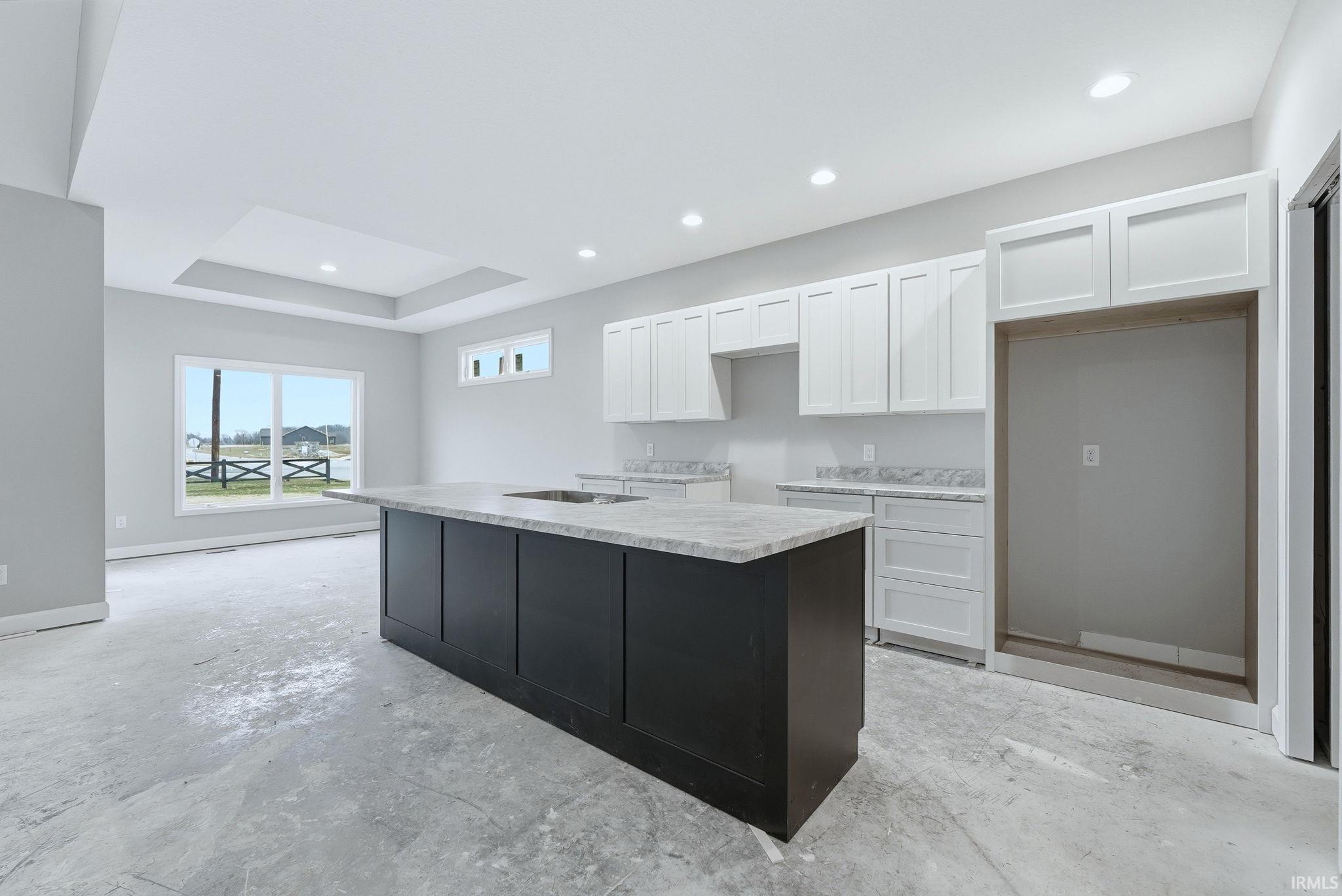 Two tone kitchen featuring unfinished concrete floors, a center island with sink, recessed lighting, two tone color scheme, and a raised ceiling