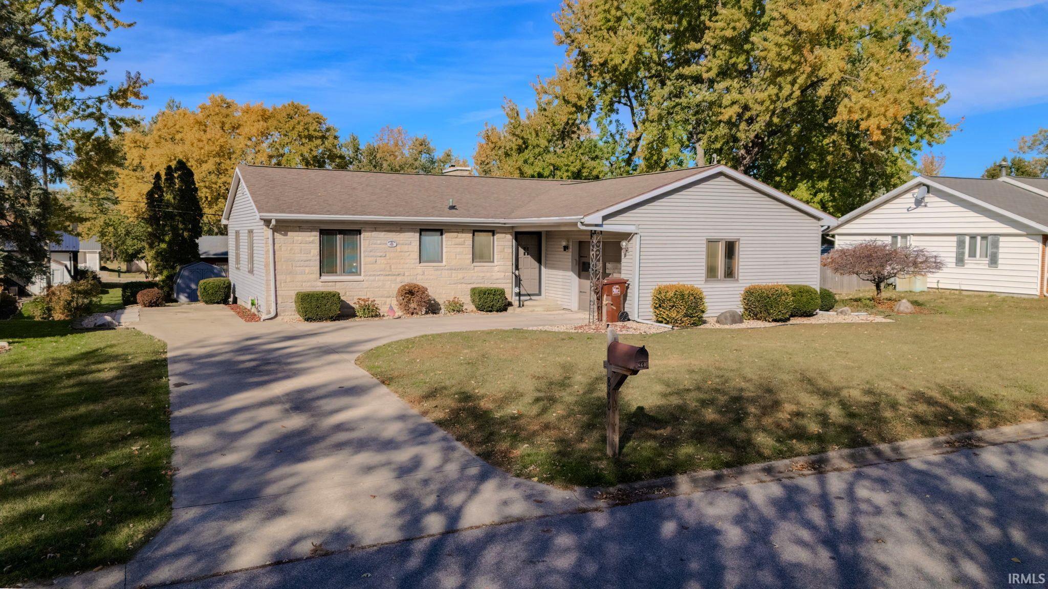 View of front of property featuring a front yard, stone siding, concrete driveway, and a chimney