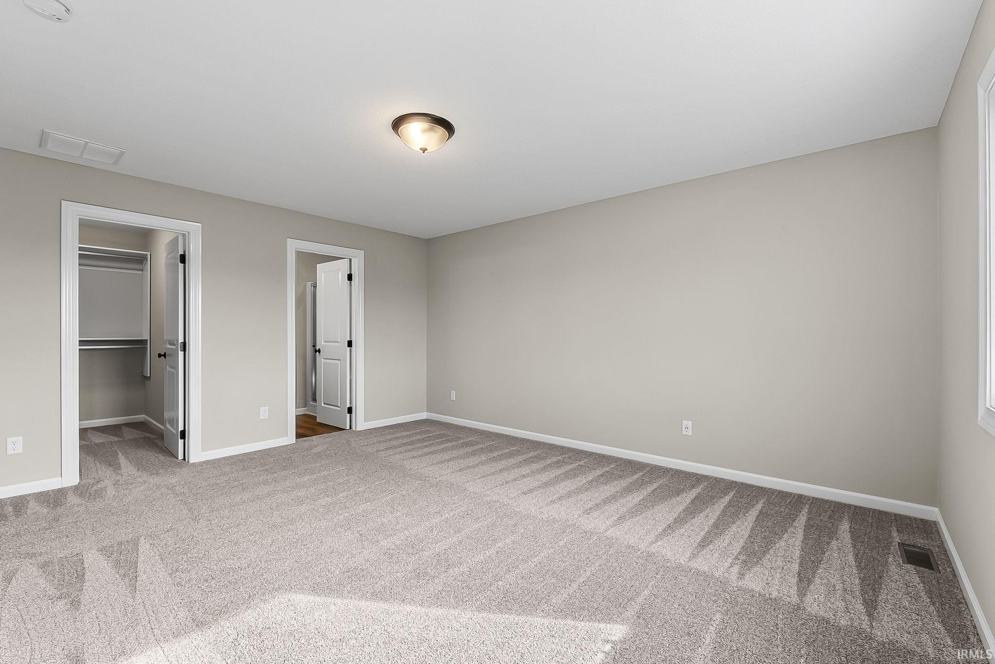 Unfurnished bedroom with a walk in closet and light carpet