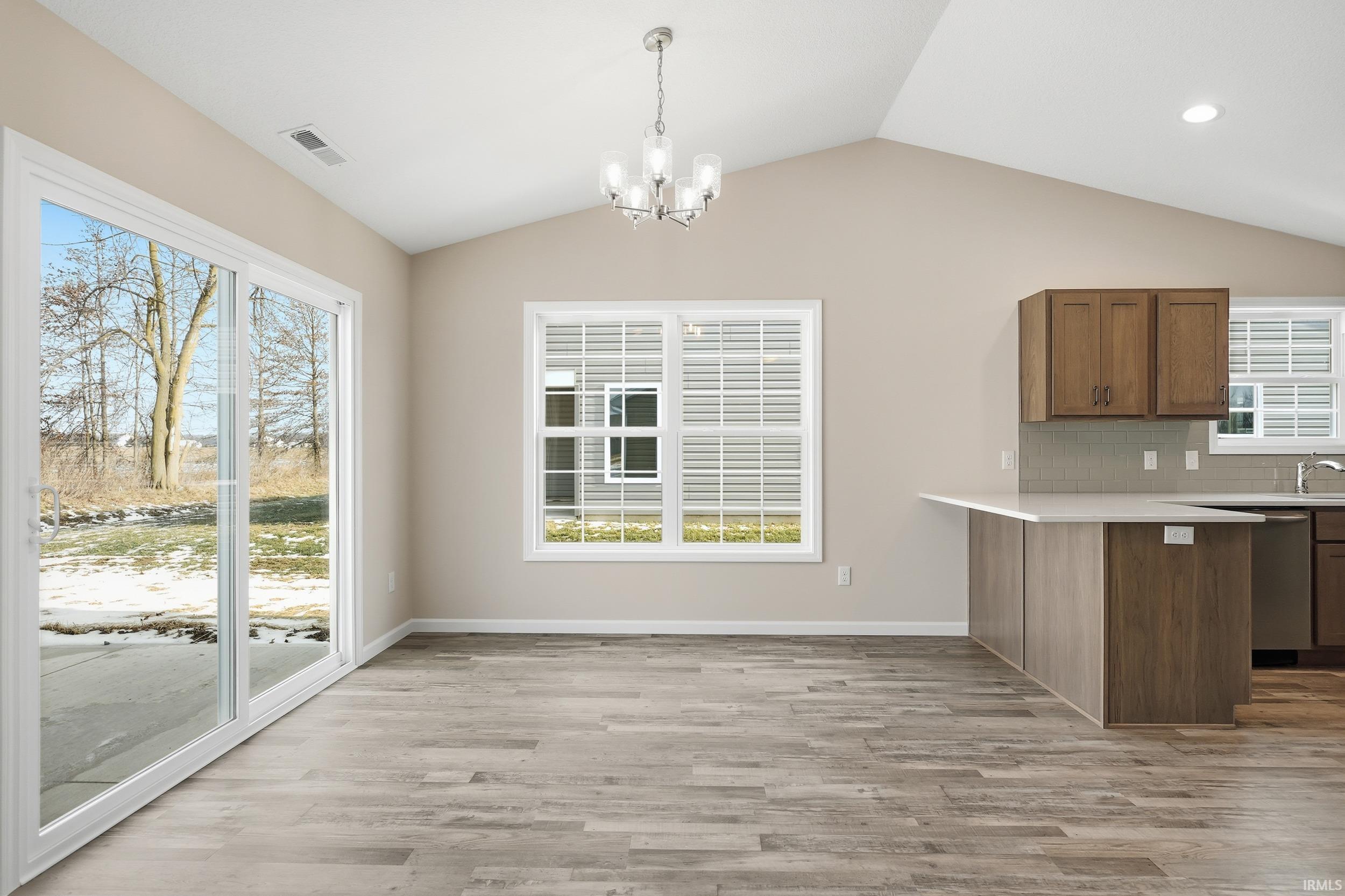 Kitchen with a chandelier, a peninsula, decorative light fixtures, light wood-type flooring, and lofted ceiling