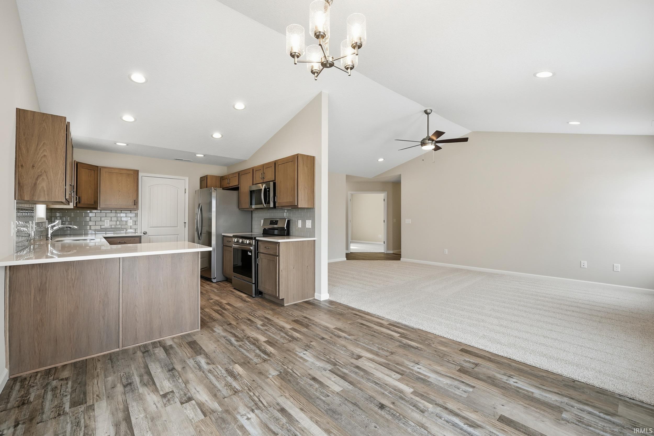 Kitchen with vaulted ceiling, tasteful backsplash, appliances with stainless steel finishes, open floor plan, and a chandelier