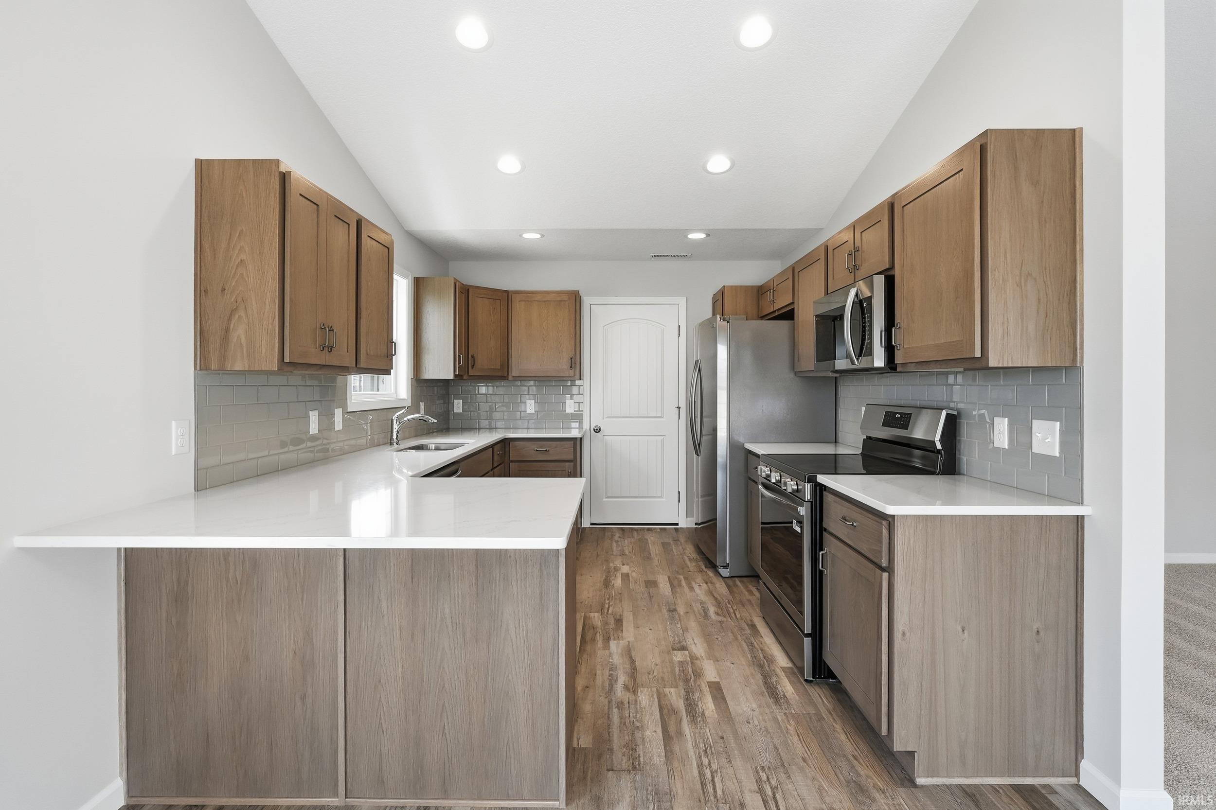 Kitchen featuring a peninsula, stainless steel appliances, decorative backsplash, vaulted ceiling, and light stone countertops