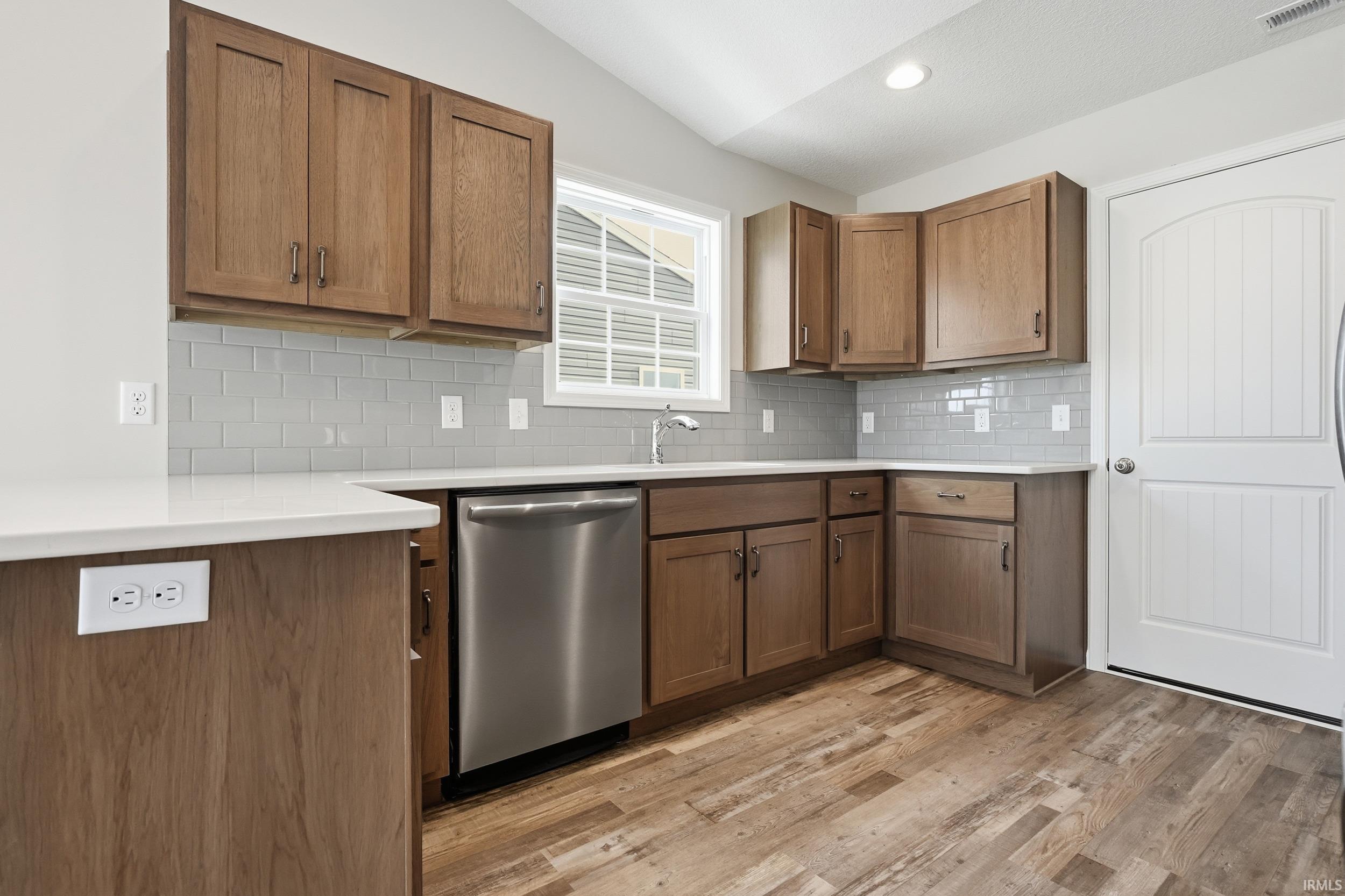 Kitchen featuring dishwasher, lofted ceiling, brown cabinets, light wood-type flooring, and backsplash