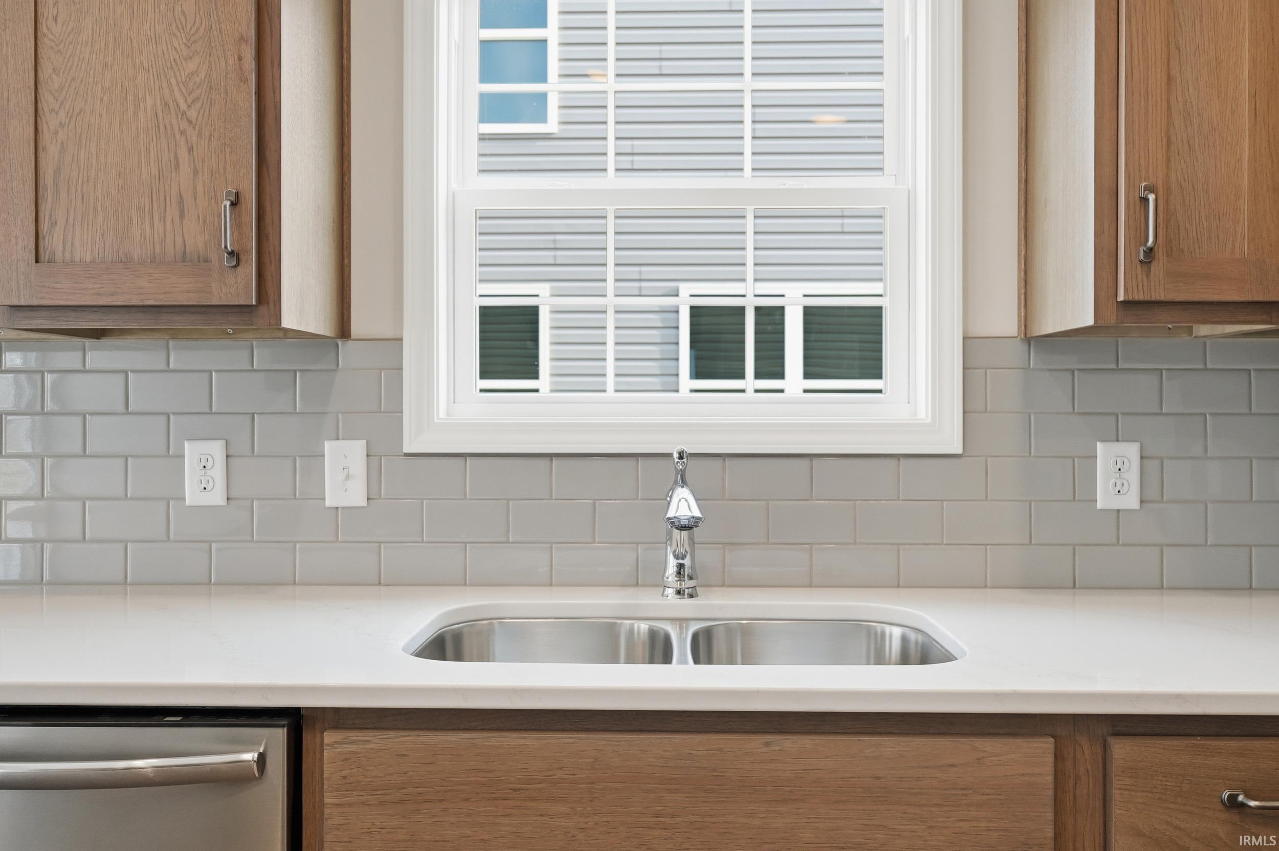 Kitchen featuring dishwasher, brown cabinets, backsplash, and light stone countertops