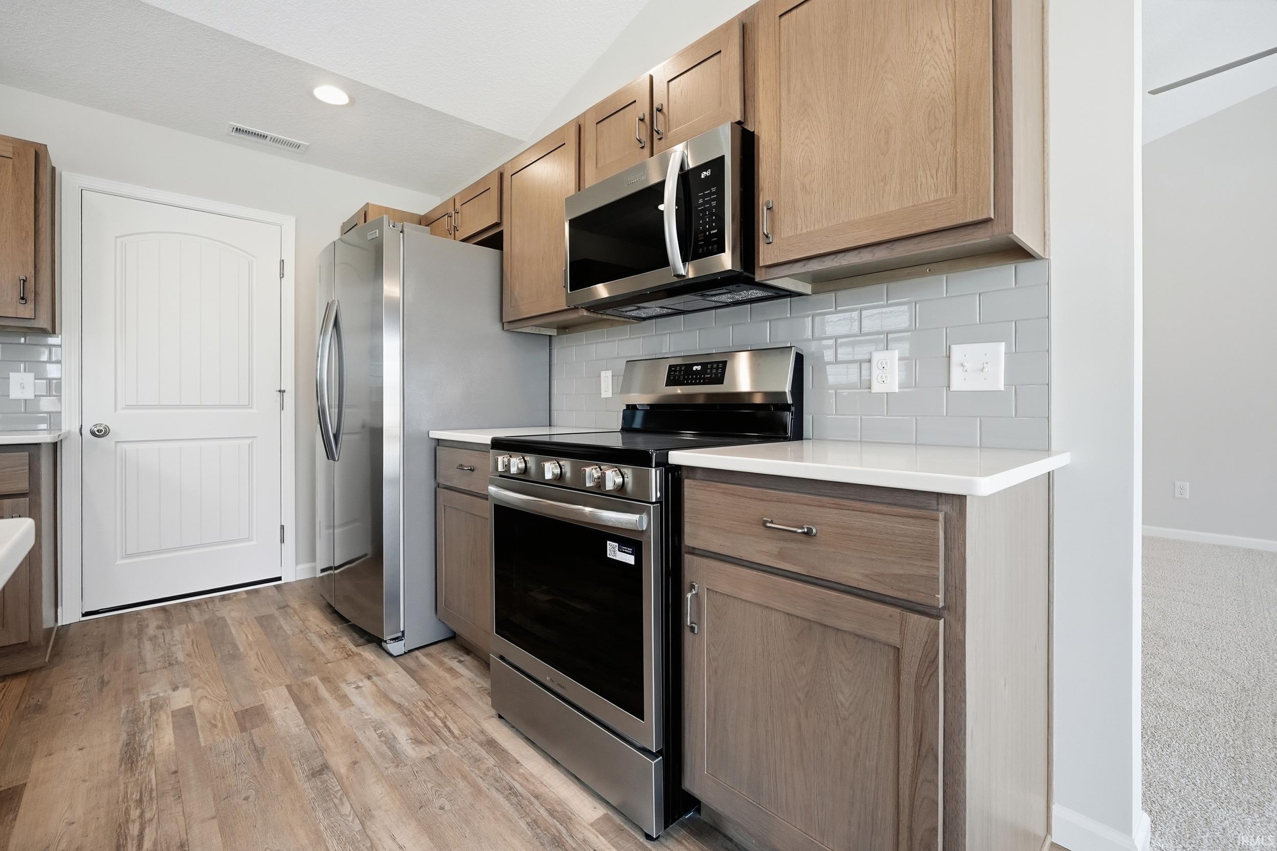 Kitchen with appliances with stainless steel finishes, light countertops, decorative backsplash, light wood-type flooring, and recessed lighting