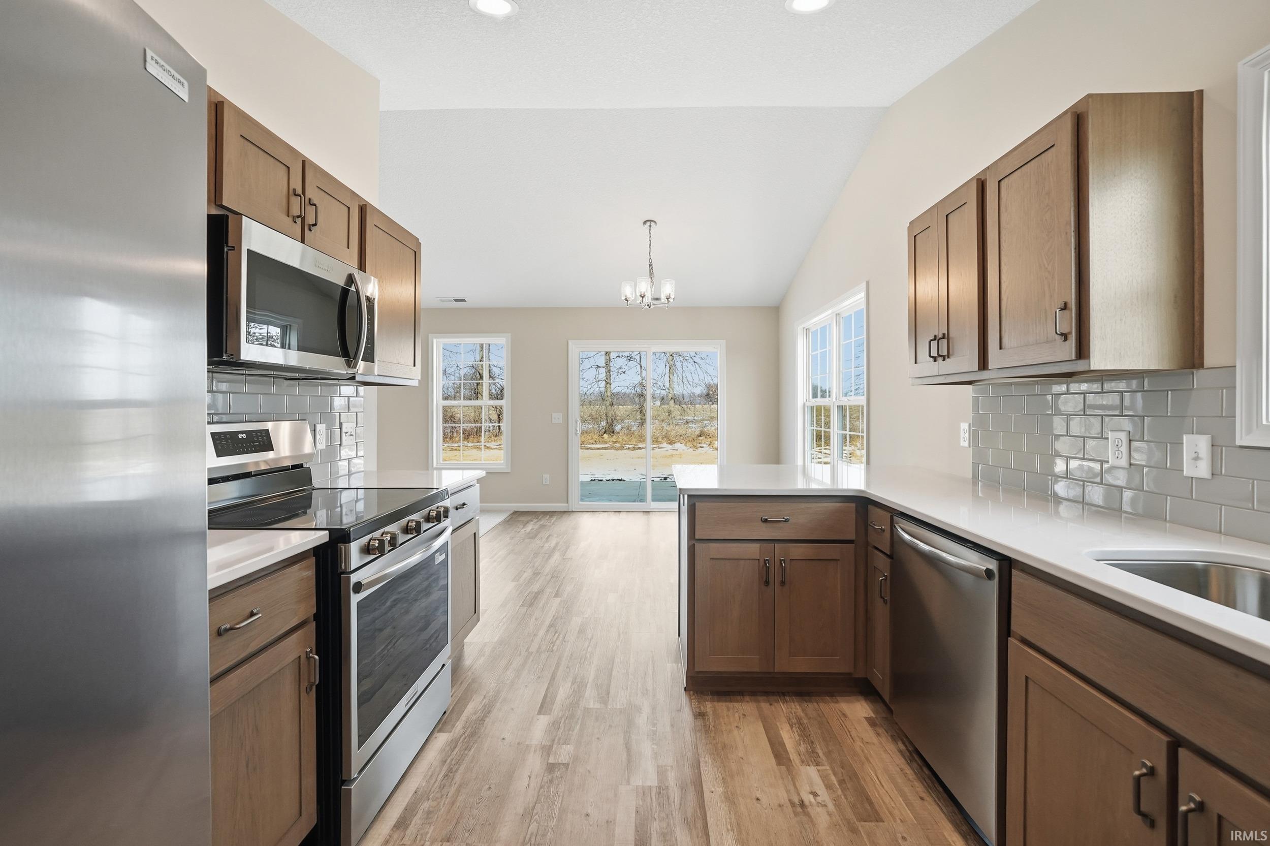Kitchen with stainless steel appliances, tasteful backsplash, light wood finished floors, a chandelier, and pendant lighting