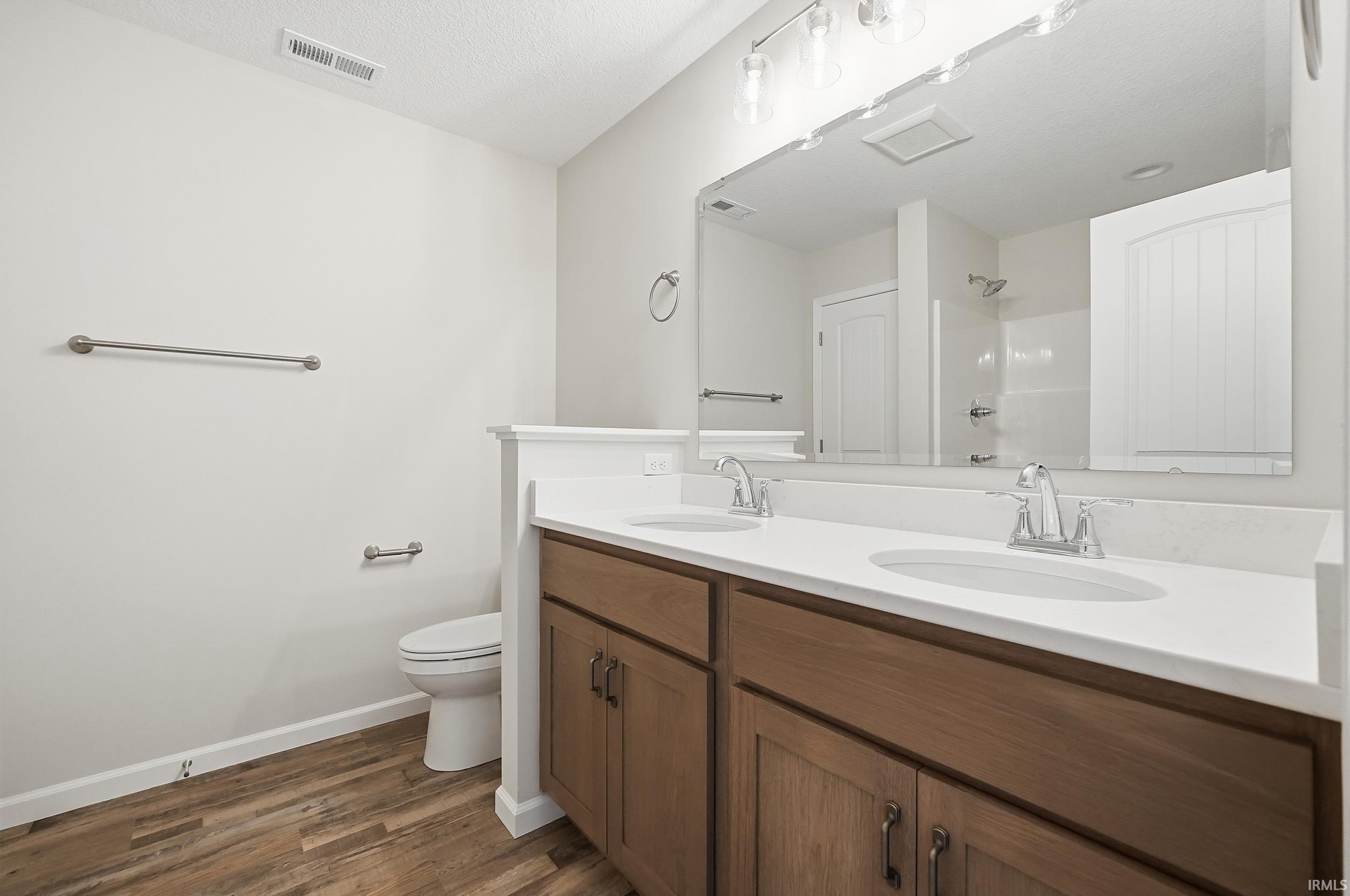 Bathroom with double vanity, a shower, and dark wood-style flooring
